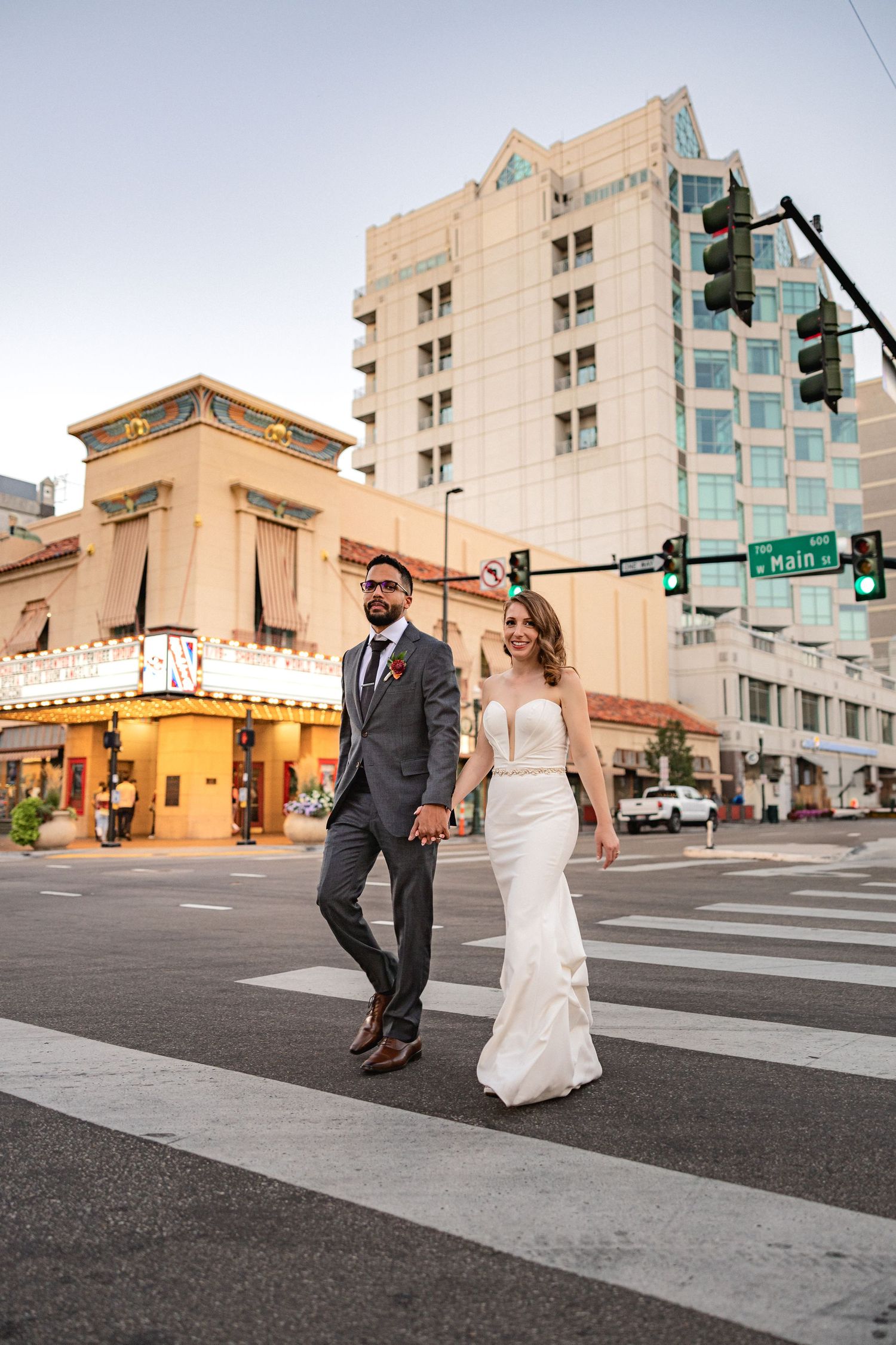 Wedding couple walks across a crosswalk in downtown Boise with historic buildings in background.