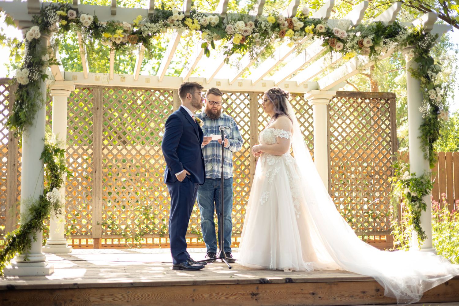 Outdoor wedding ceremony setup with white lattice backdrop and floral decorations in natural lighting.