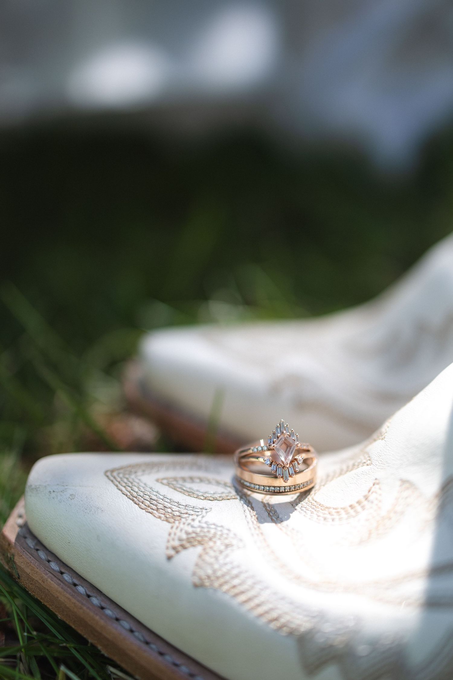 Wedding rings arranged artistically on vintage white bridal shoes in grass.