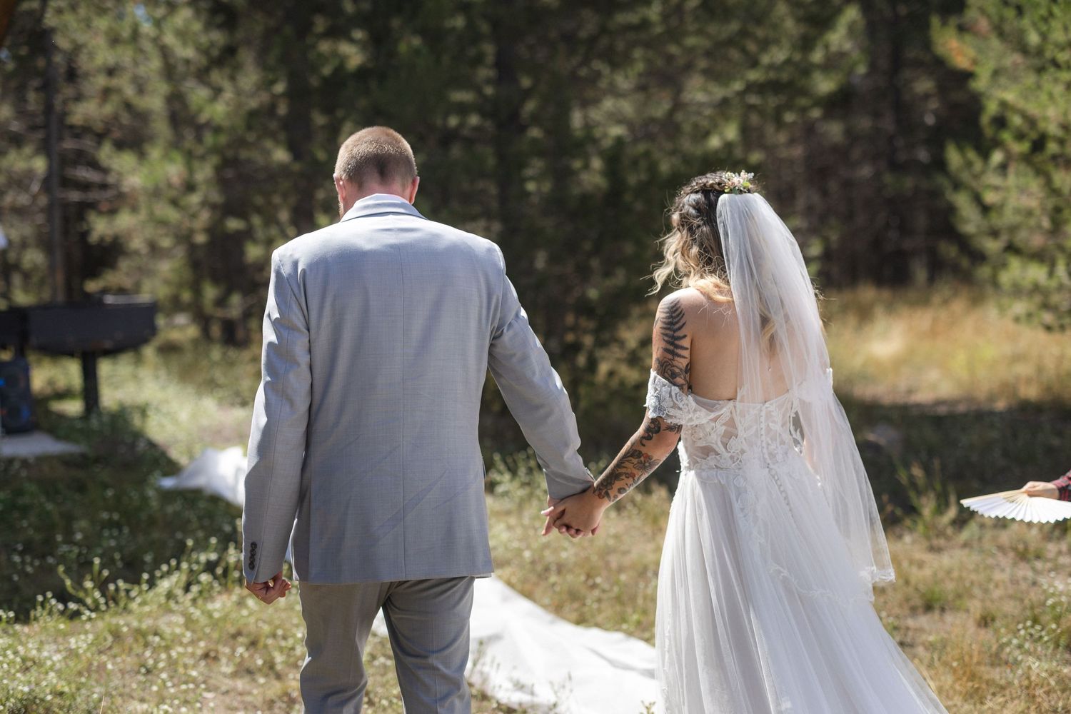 Wedding couple walking hand in hand through mountain meadow after ceremony.
