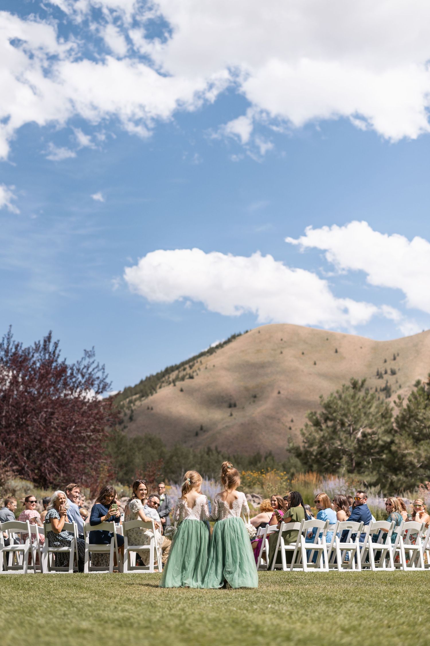 Outdoor wedding ceremony setup with white chairs on grass against mountainous landscape.