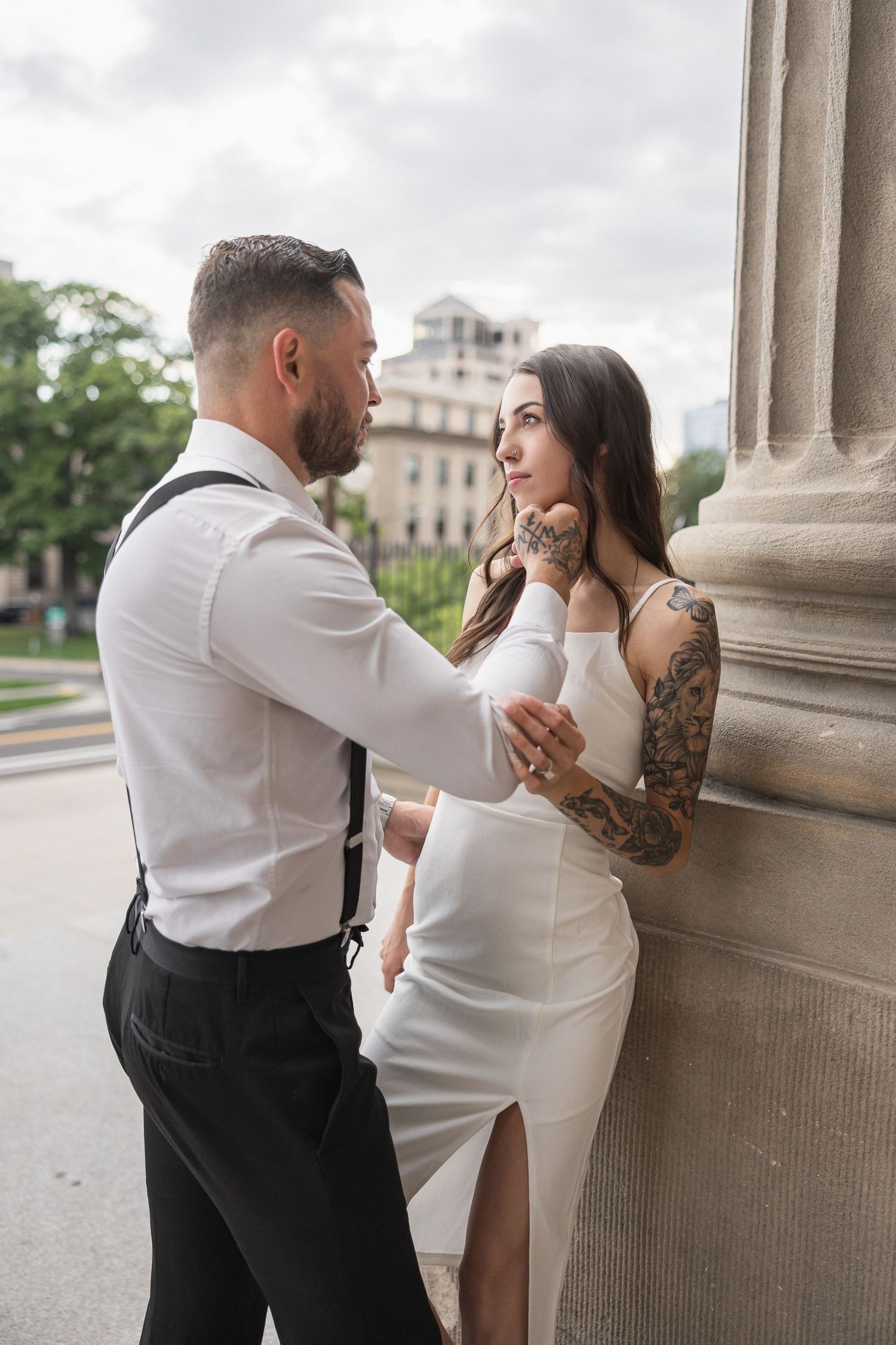 A couple shares an intimate moment against a stone column outdoors.