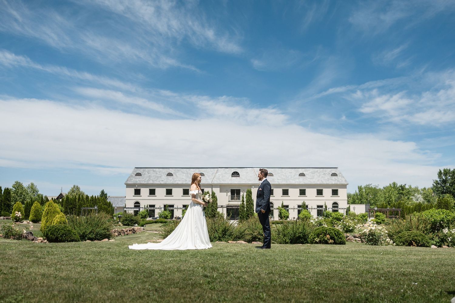 A panoramic view of a white building and expansive lawn under a bright blue sky.