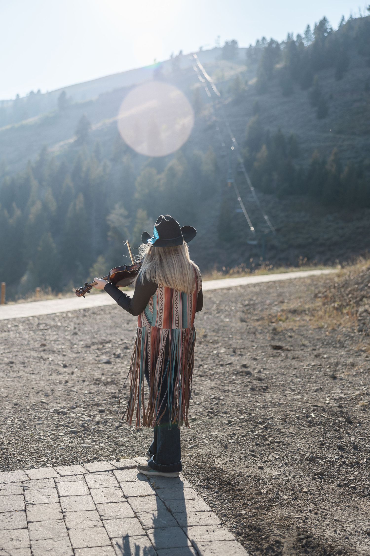 Person playing violin on mountain path during golden hour.