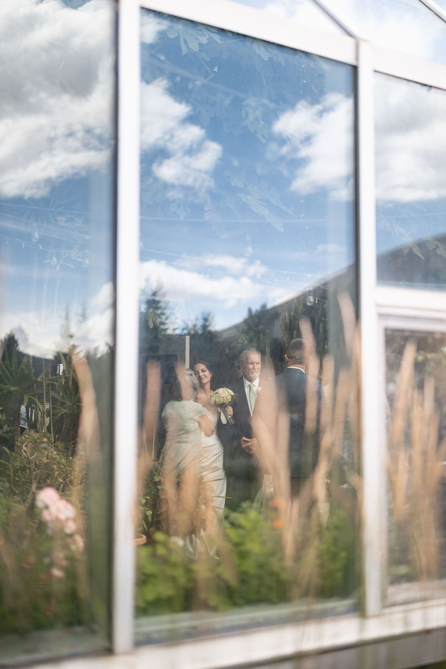 Panoramic view through greenhouse windows showing mountain landscape and blue sky.