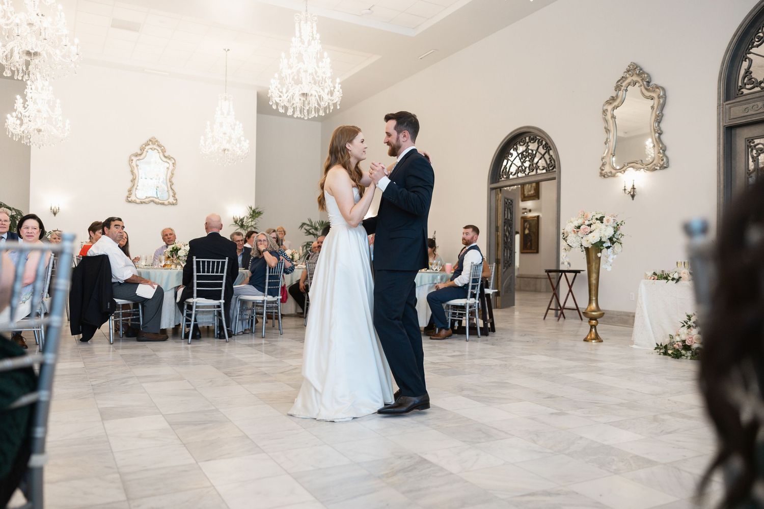 Wedding reception venue with crystal chandeliers and elegant white decor.