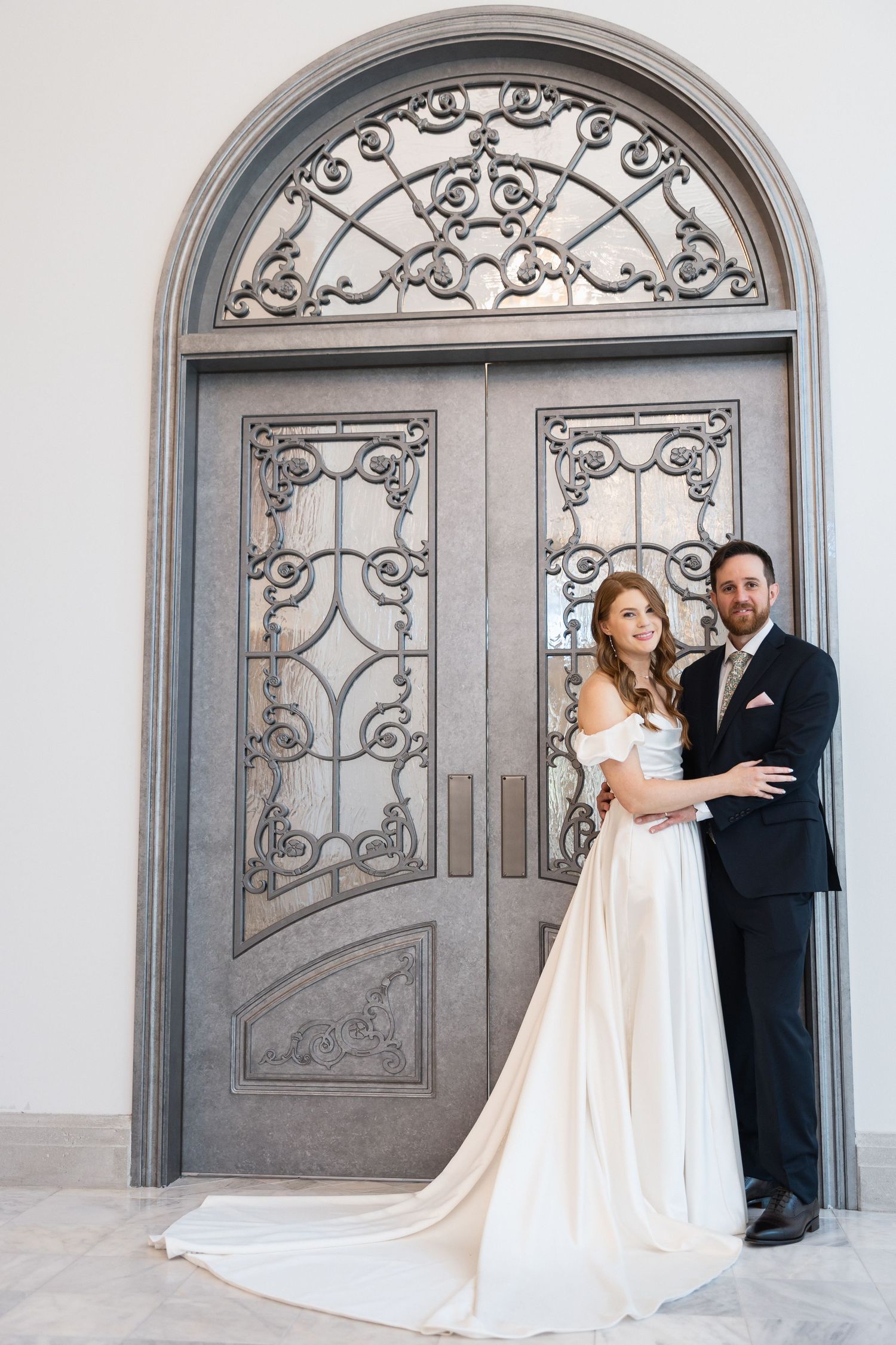 Elegant couple poses in front of ornate grey double doors for wedding photos.
