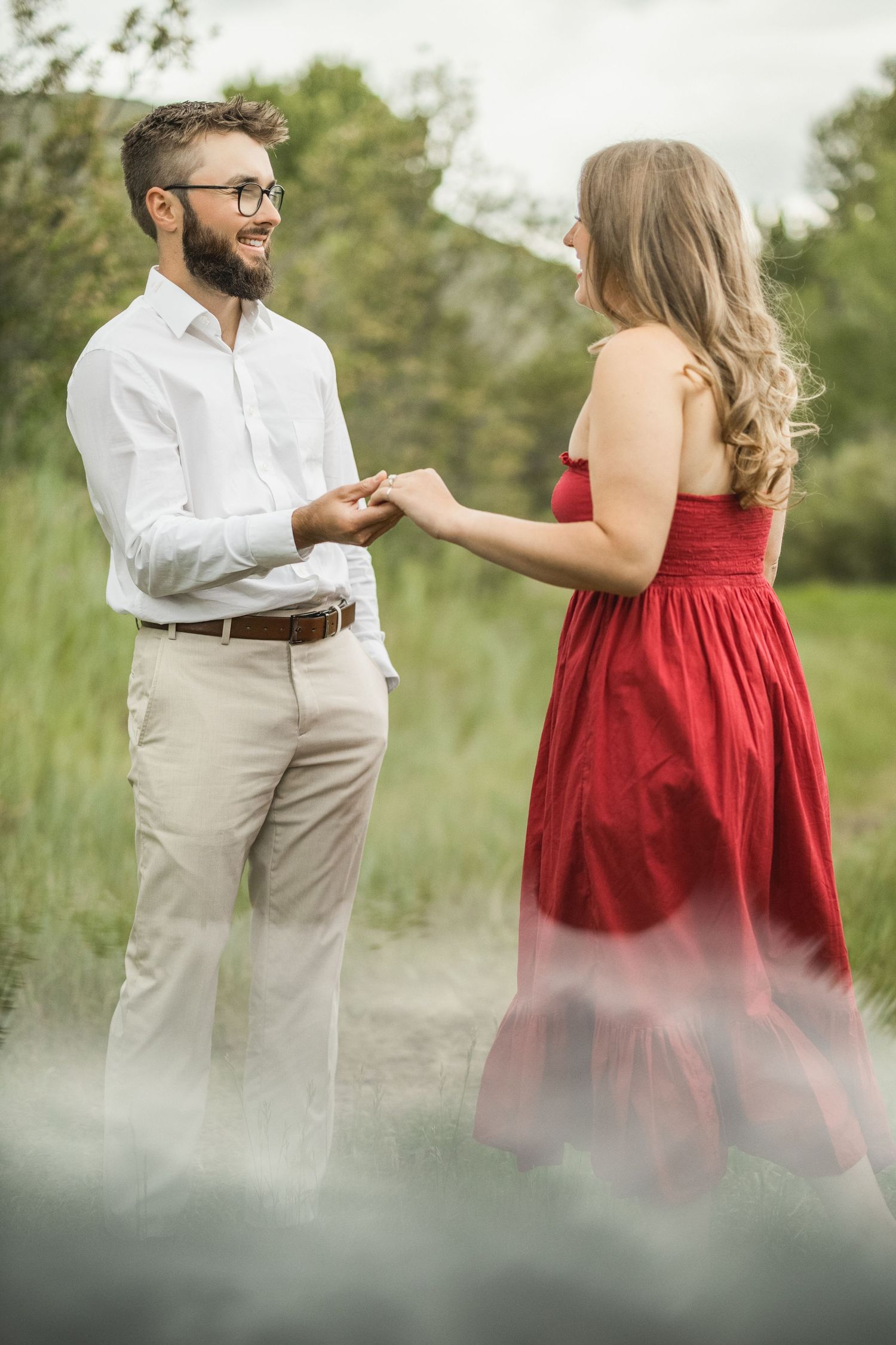 Two people sharing a tender moment outdoors, with one wearing a red dress and the other in a white shirt and khakis.