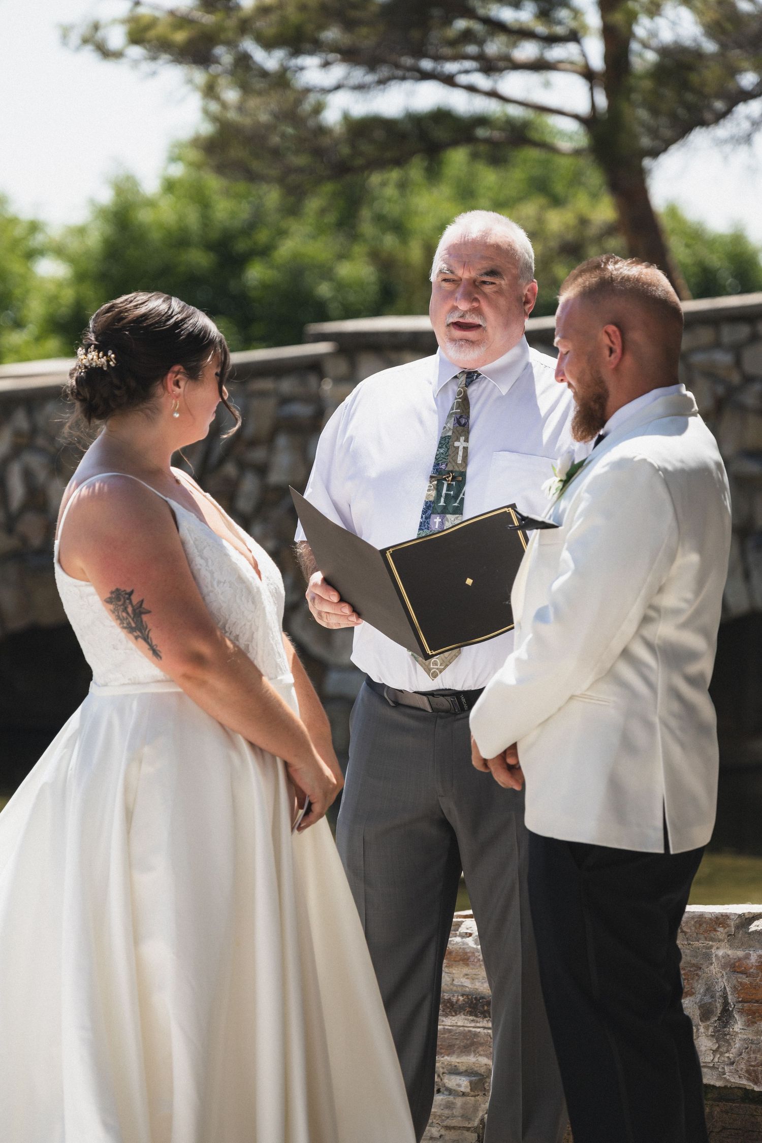 A couple and officiant stand together during an intimate outdoor wedding ceremony.