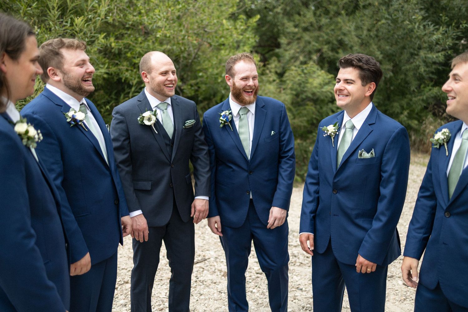 Candid moment of groomsmen laughing together in navy suits outdoors.
