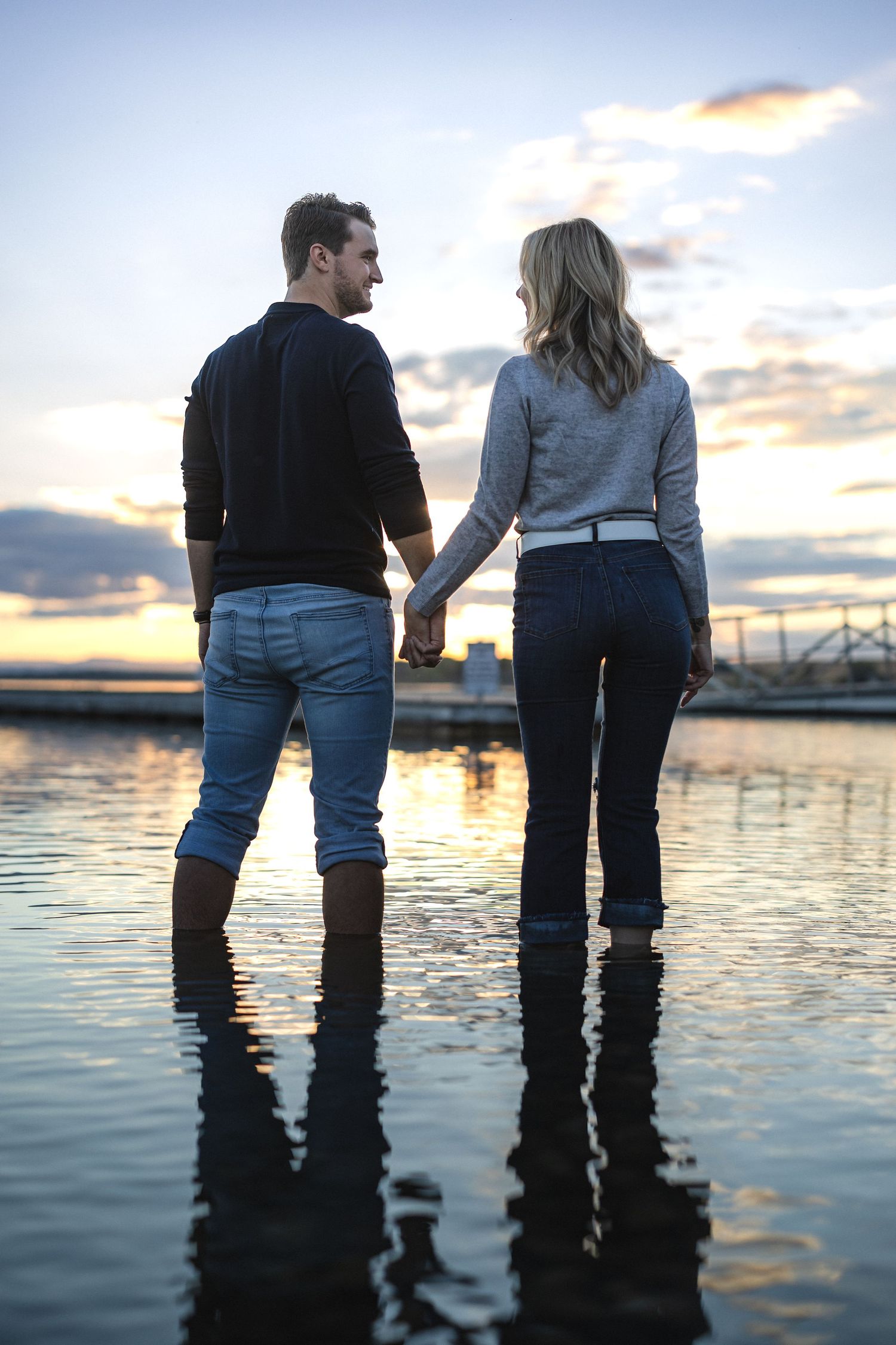 Couple in boots standing together in calm water during golden hour.