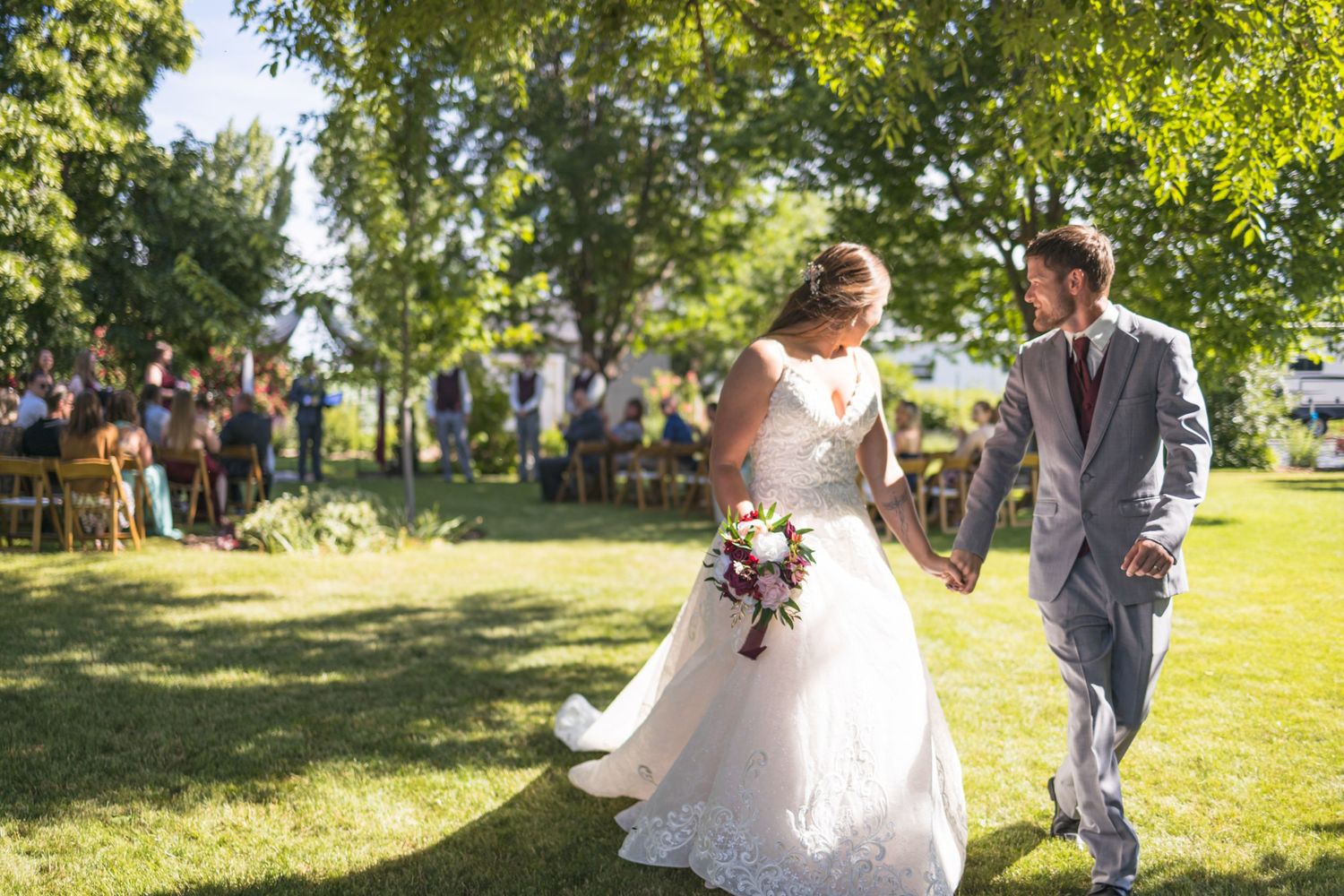 Sunlit wedding ceremony exit with couple walking hand in hand through an outdoor garden venue.