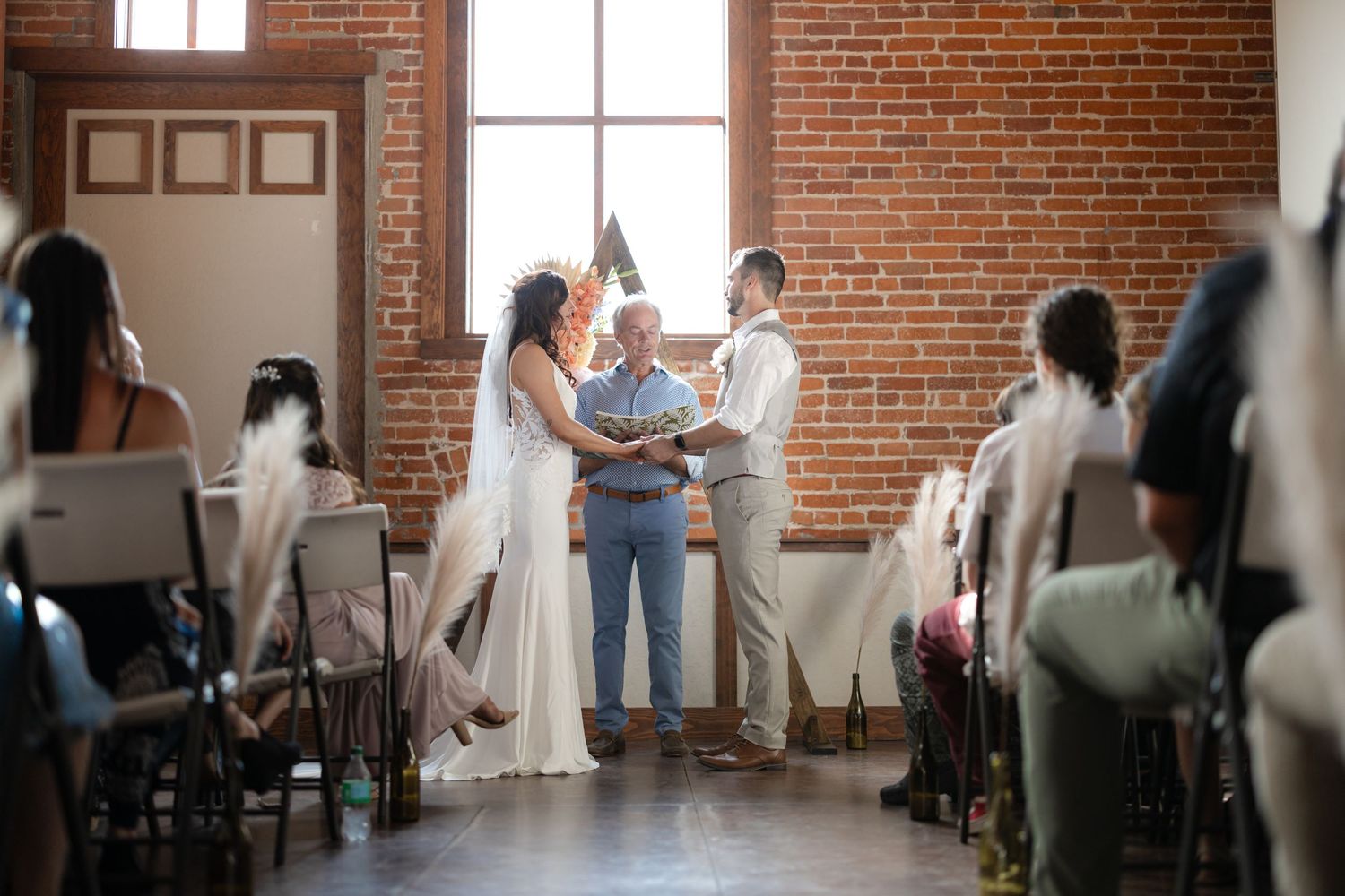 Intimate indoor wedding ceremony with exposed brick walls and wooden beams overhead.