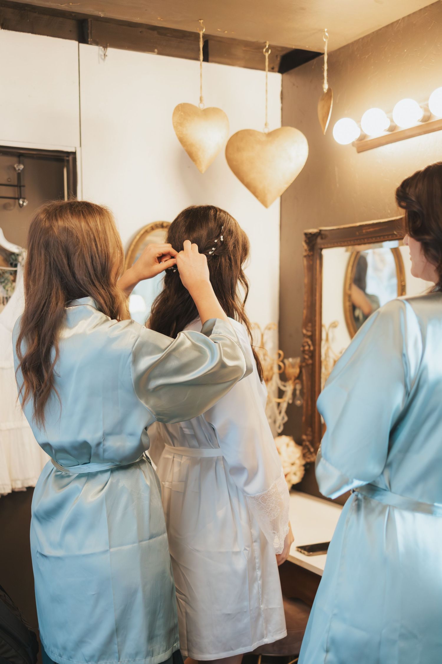 Wedding preparation scene with robed figures styling hair under gold heart decorations.