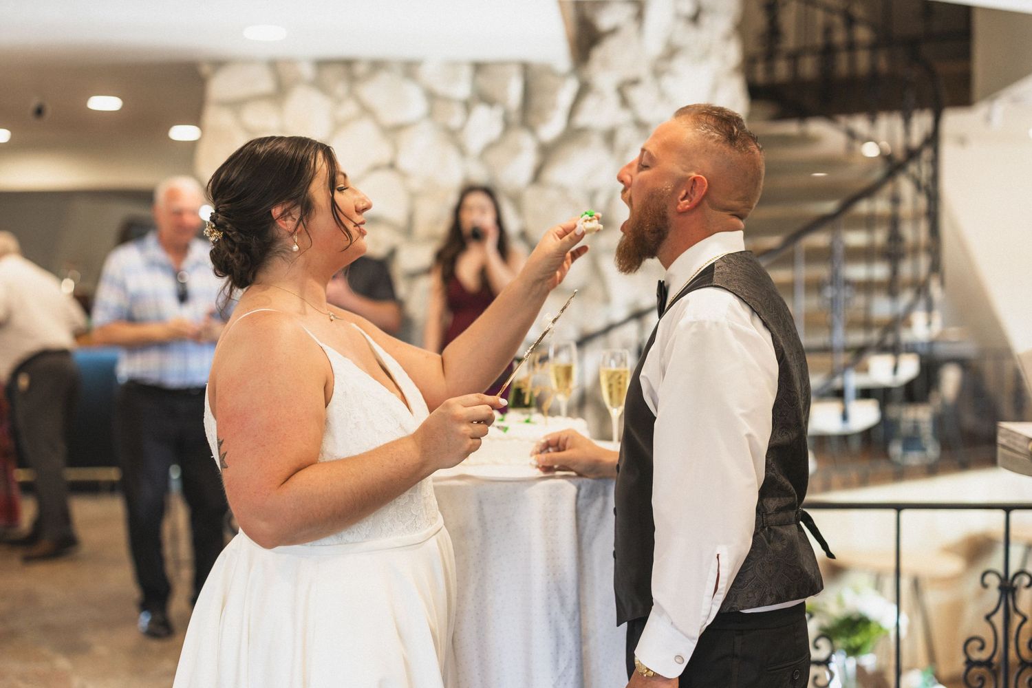 Newlyweds share a lighthearted moment while feeding each other cake at their wedding reception.