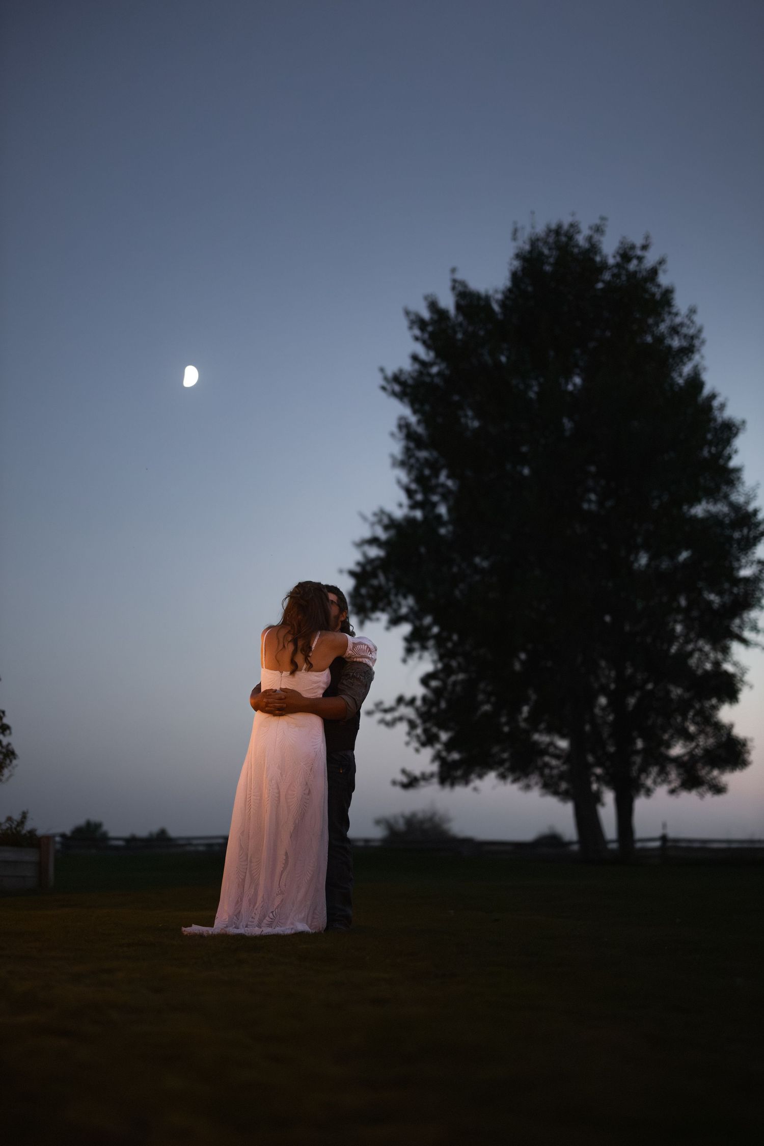 Silhouettes of a couple embrace under a moonlit sky with trees in the background creating a romantic atmosphere.