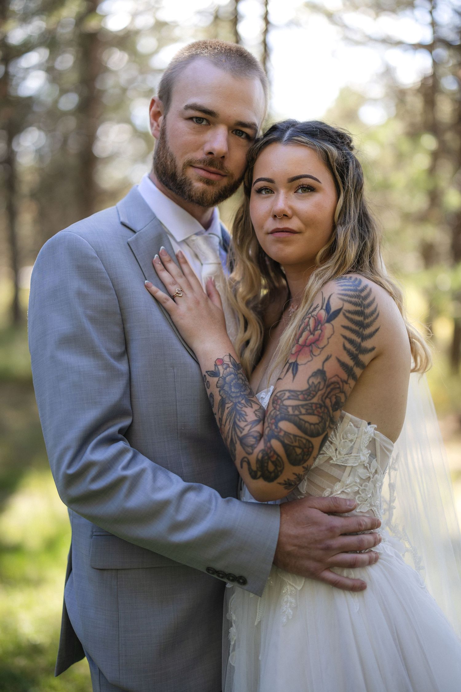 Wedding portrait in forest with bride in white gown showing artistic tattoo sleeve.