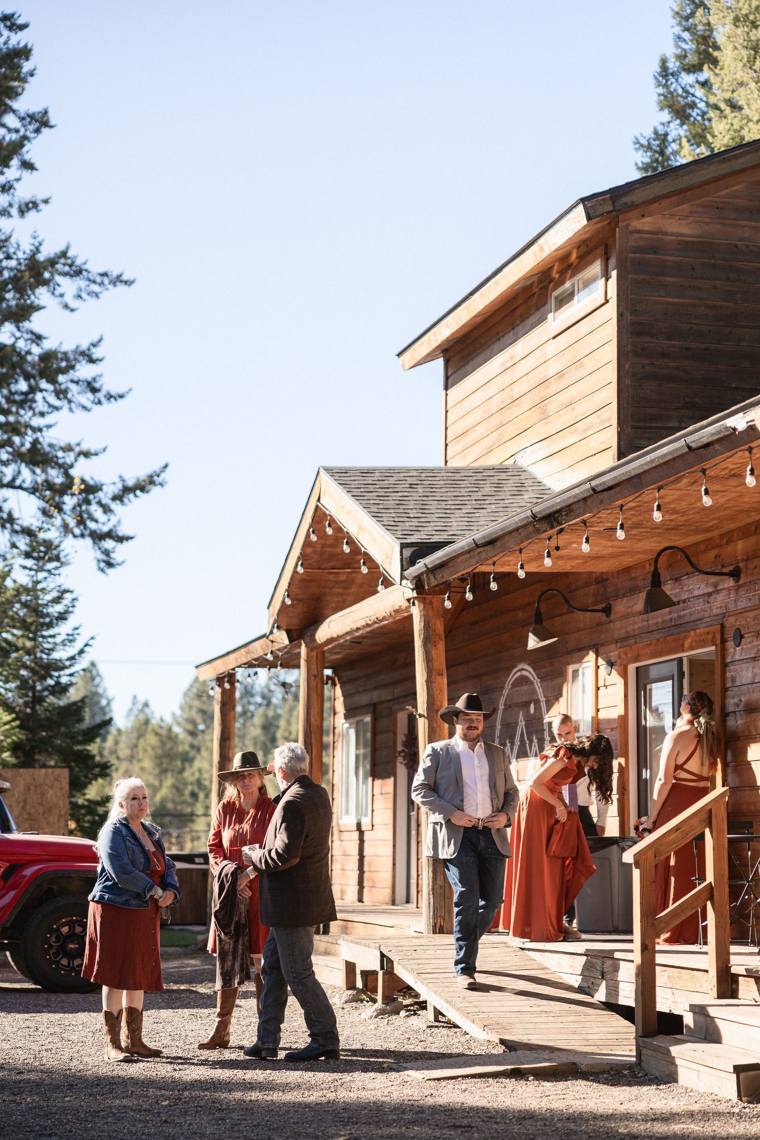 Rustic wooden lodge venue with string lights and wedding guests gathered on the front porch.