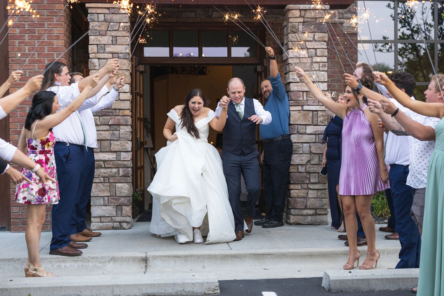 Wedding couple exits through a tunnel of guests at a brick venue entrance.