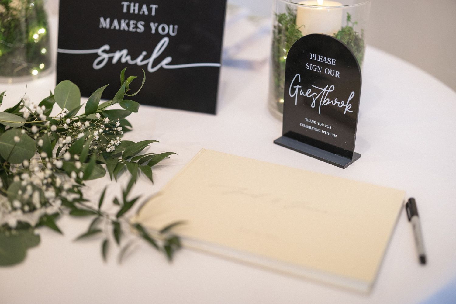 Wedding guest book table decorated with greenery and black signs with elegant script.