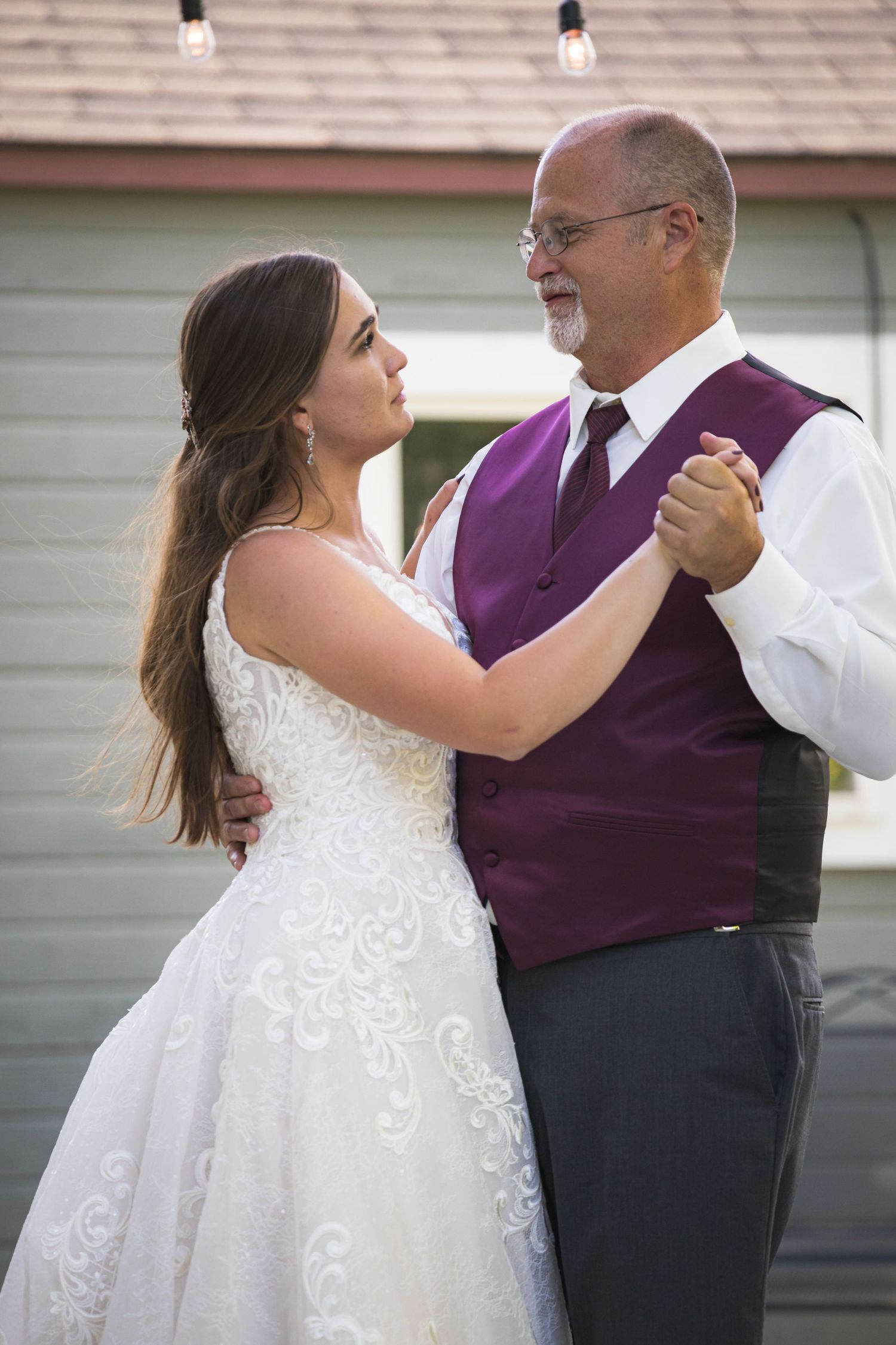 A couple shares a wedding dance together, with the person wearing a purple vest and white shirt.