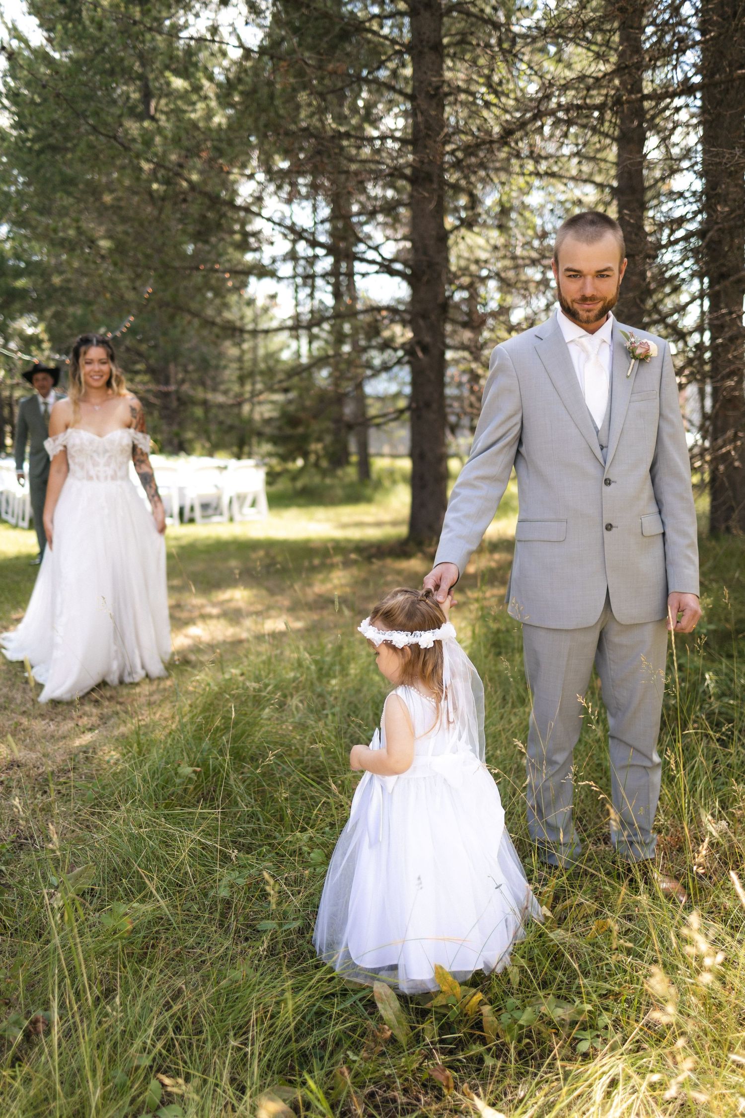 Sweet family moment with flower girl between bride and groom in pine forest setting.