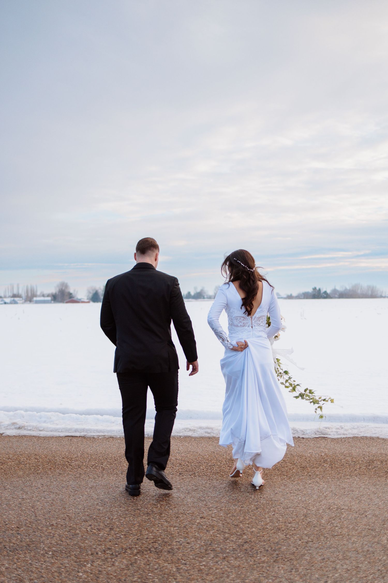 Couple walking along snowy beach with flowing white dress and winter landscape.