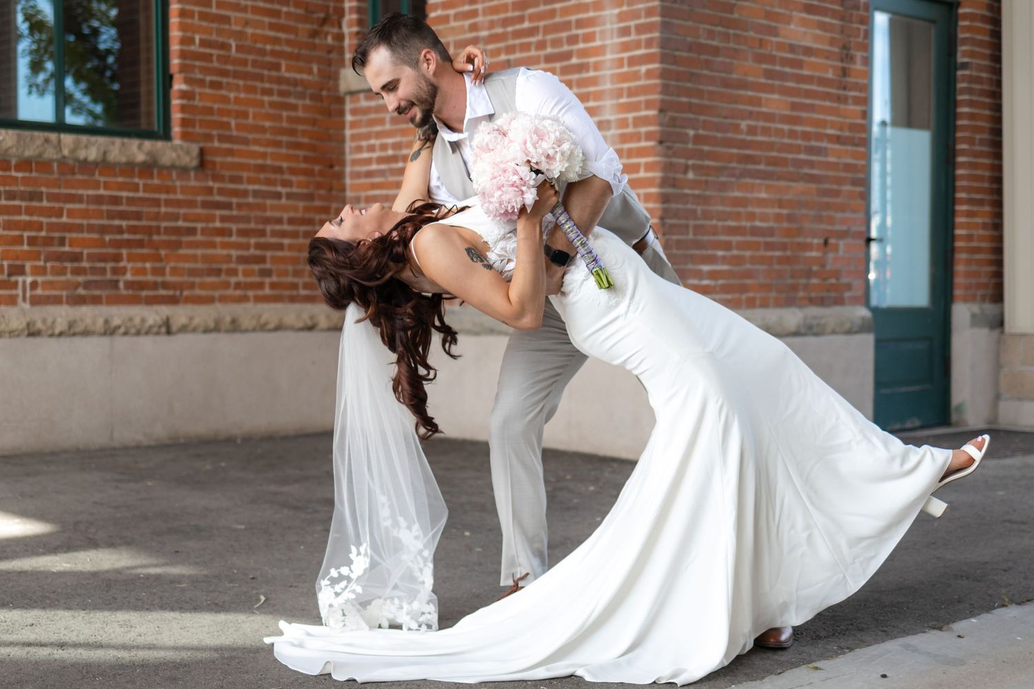 Romantic wedding dip pose against architectural brick backdrop.