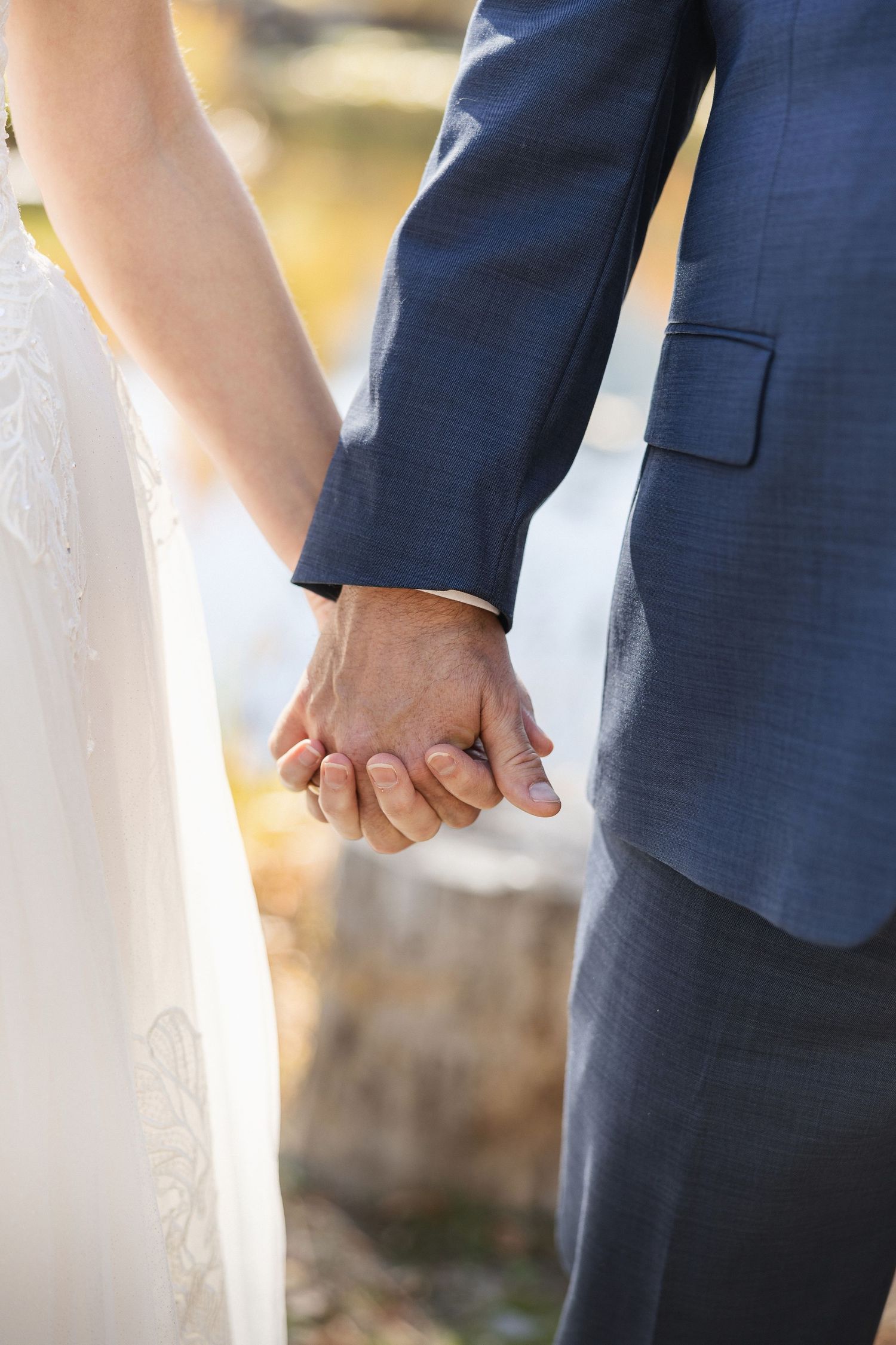 Close-up of newlyweds holding hands against a scenic fall backdrop.