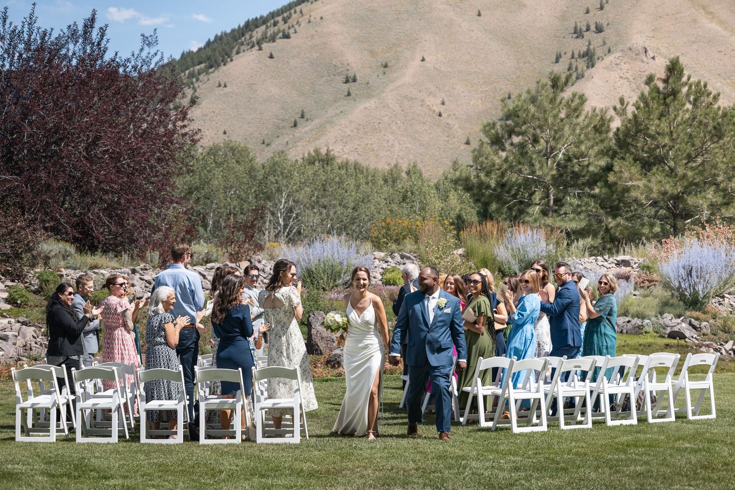 Panoramic view of wedding ceremony setup with white chairs against mountainous landscape.