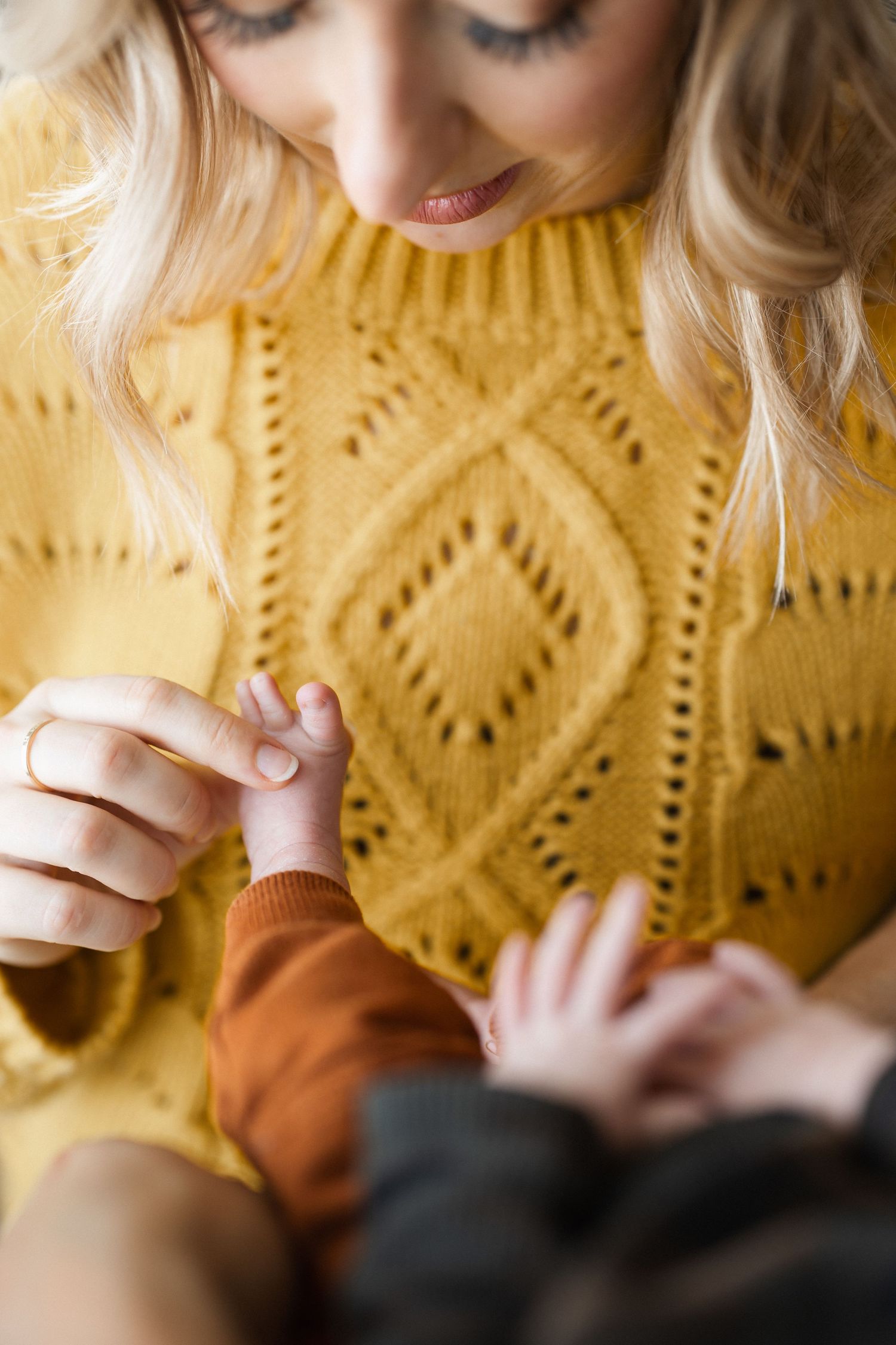 Someone wearing a yellow knit sweater with a diamond pattern holds something small in their hands.