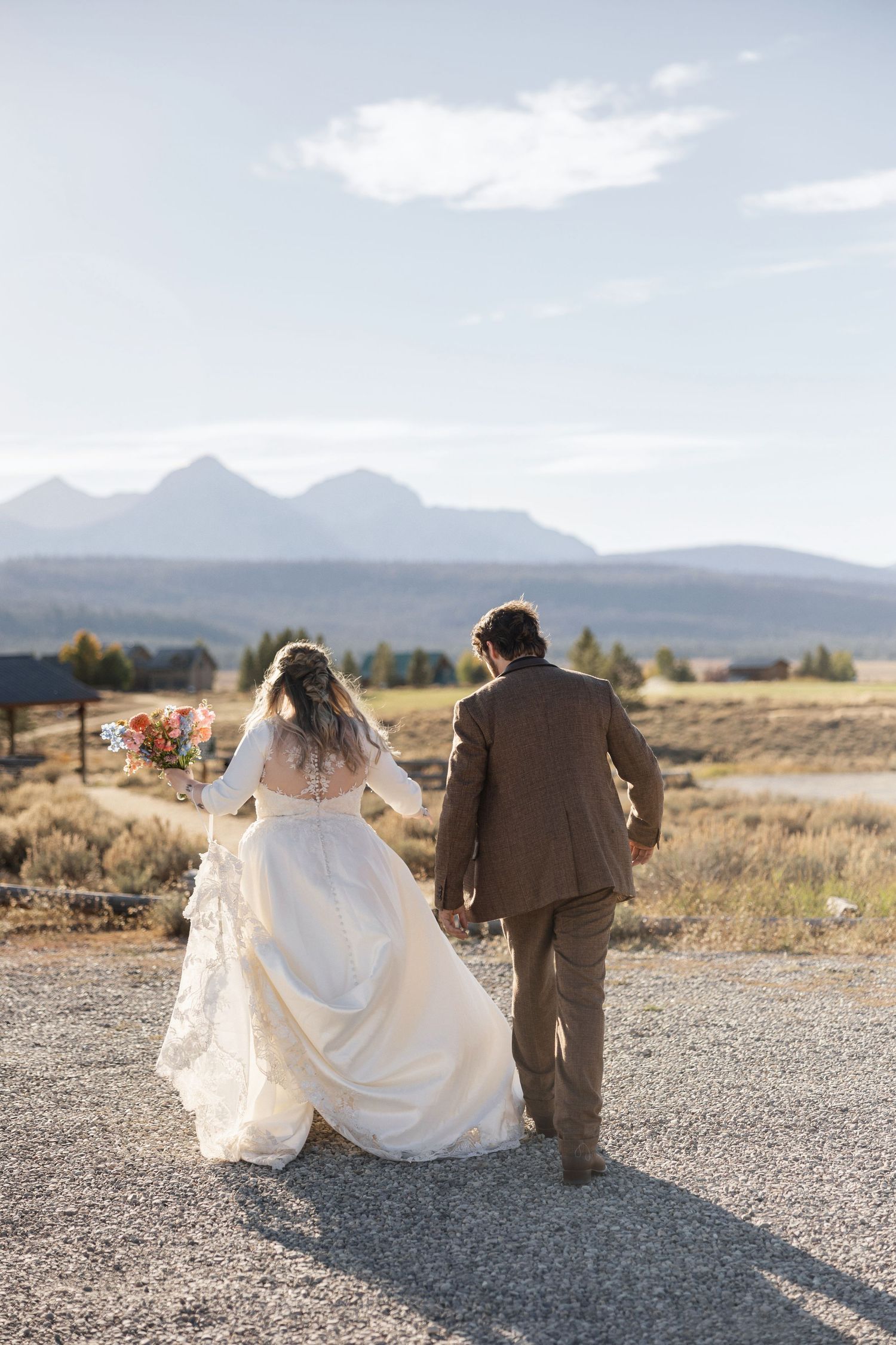 Newlyweds walking together on a desert path with dramatic mountain scenery.