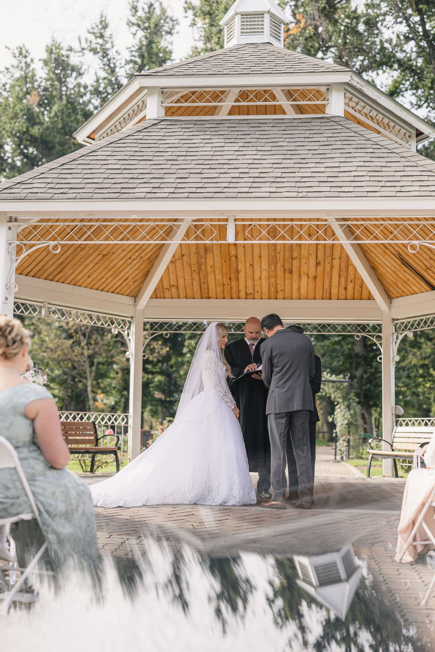 Wedding ceremony taking place under wooden gazebo with ornate roof details.