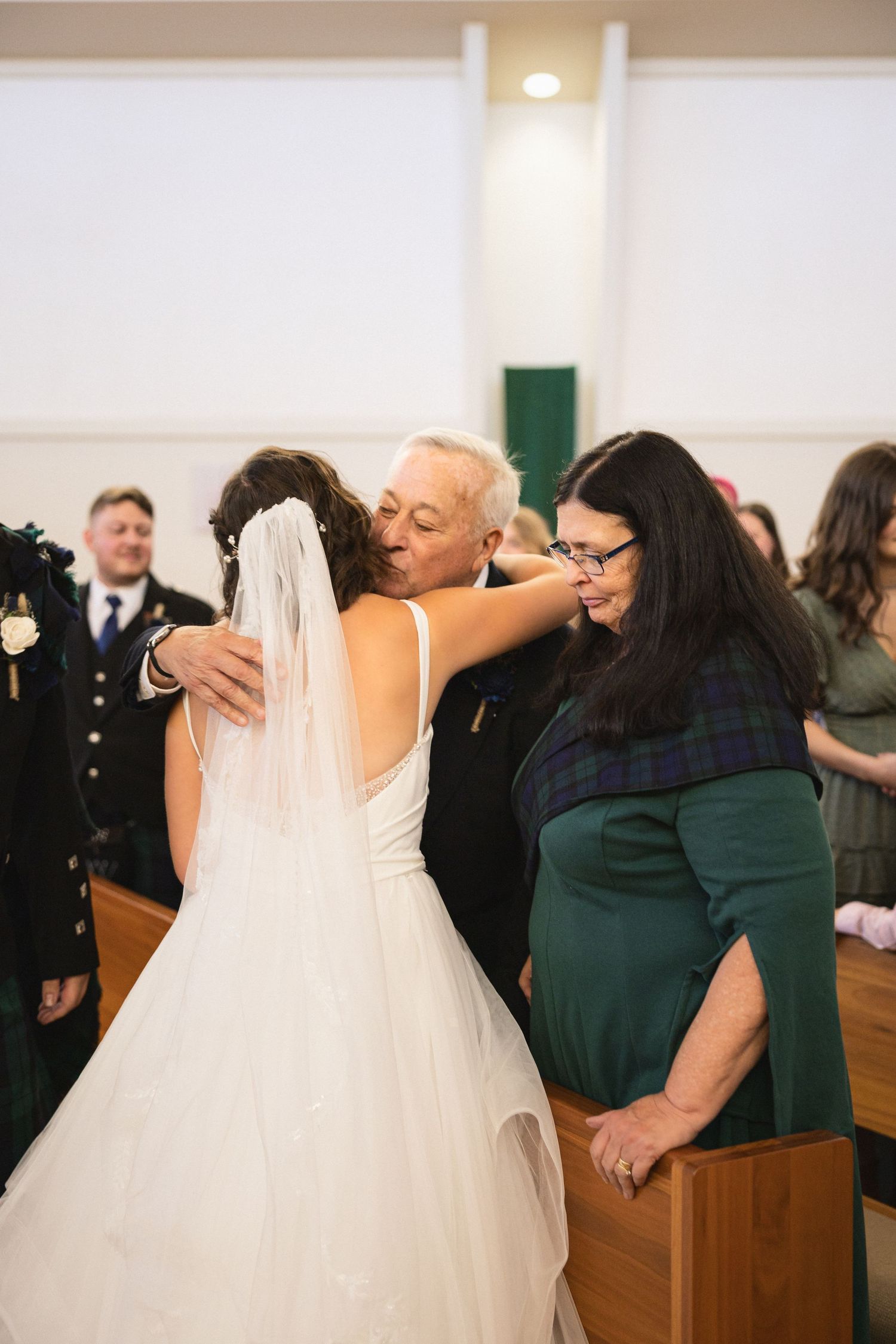 Wedding guests embrace at a church ceremony while wearing formal attire and smiles.