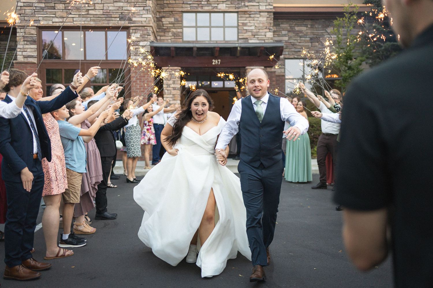 Wedding couple walks through guest sendoff line outside brick venue entrance.