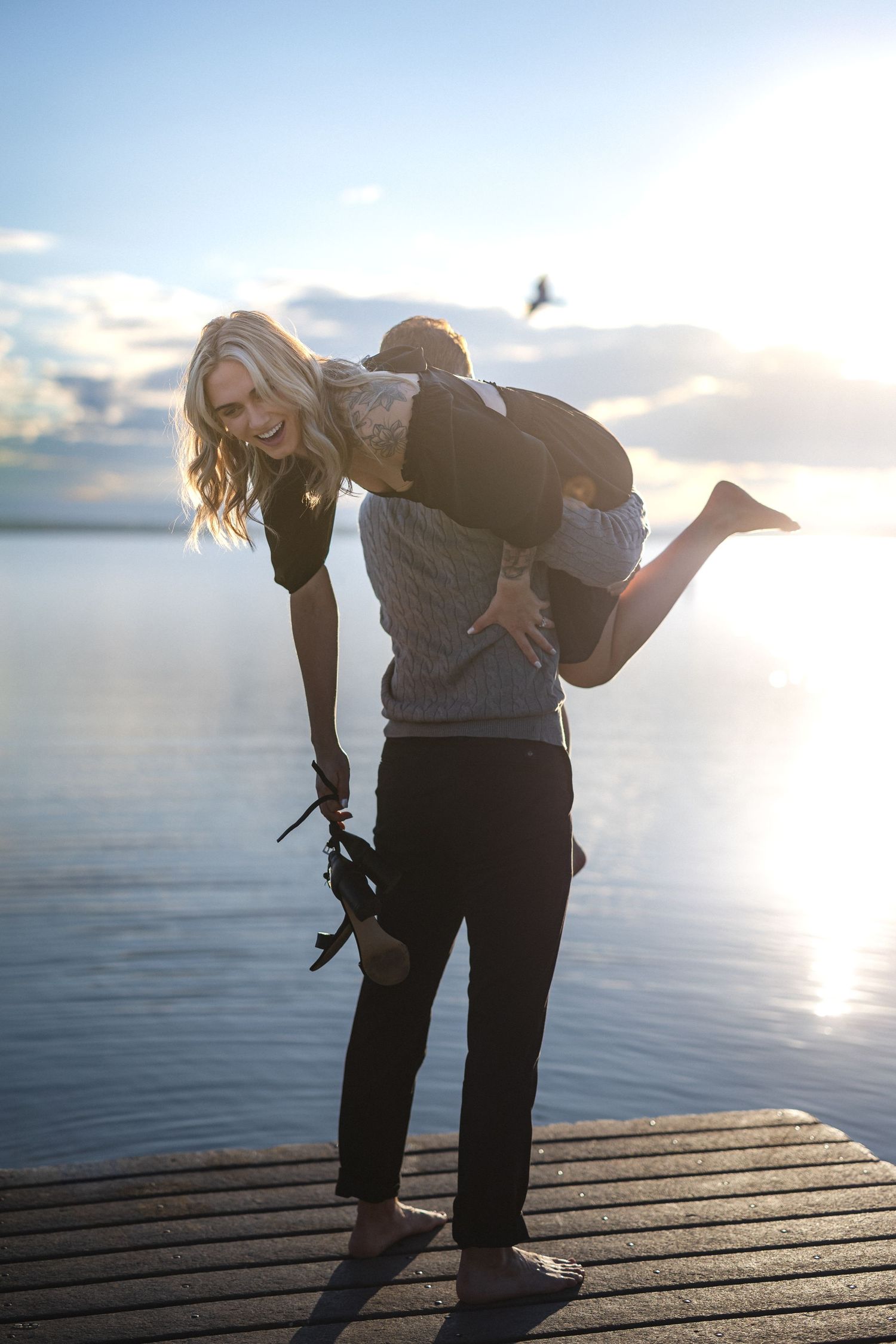 A playful piggyback moment captured on a wooden dock at sunset with calm water in the background.