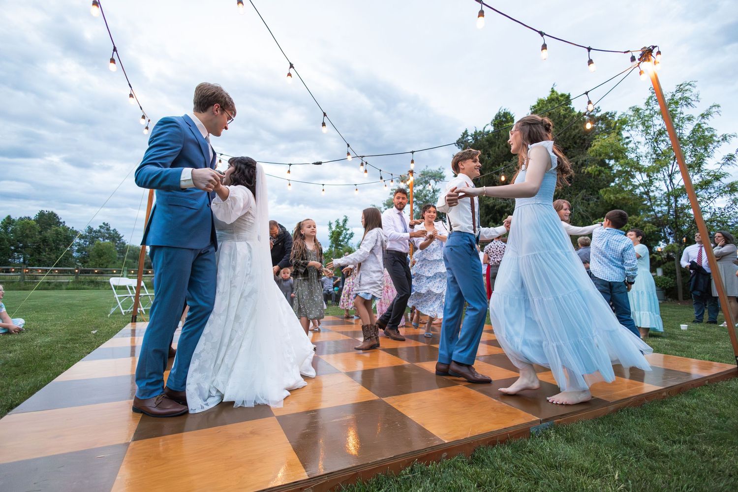 Multiple couples dancing on a wooden outdoor dance floor at a wedding reception.