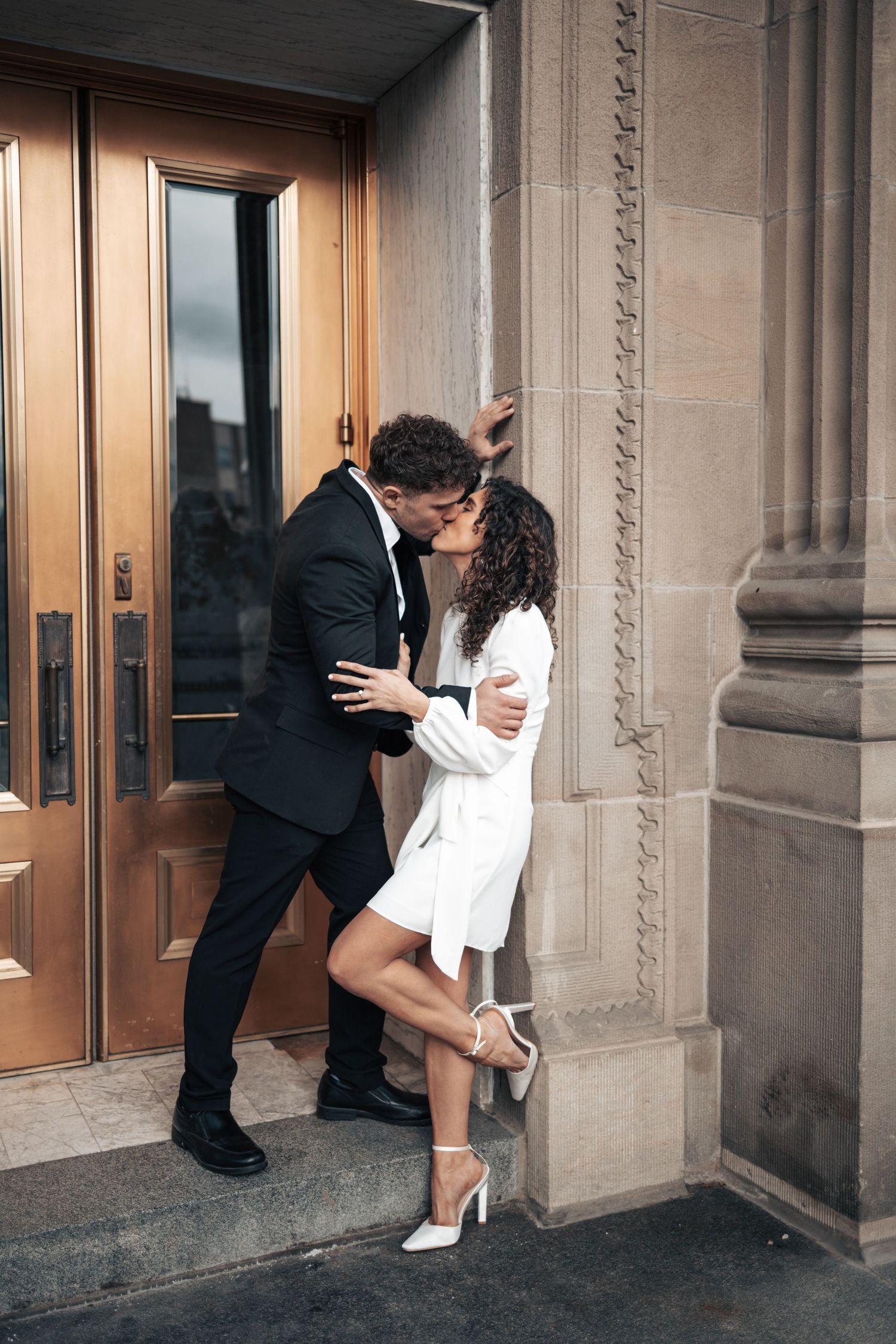 Intimate moment between couple in formal wear against classical building exterior.
