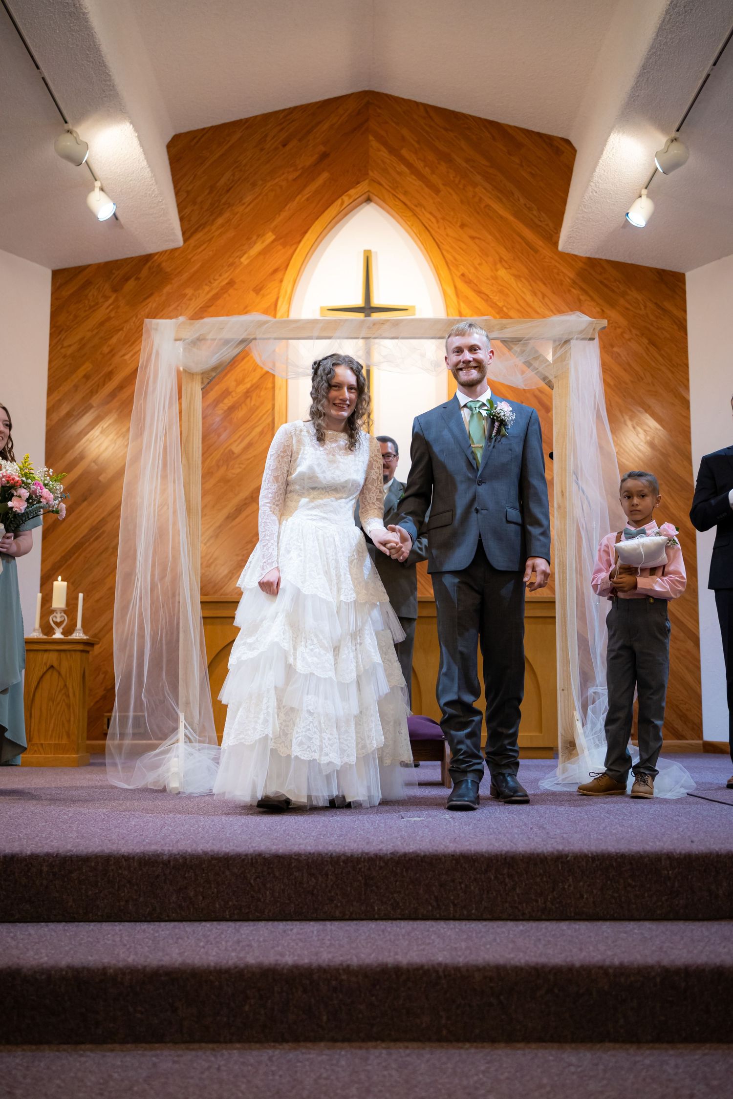 Wedding couple standing at church altar with decorative cross and wooden paneling.