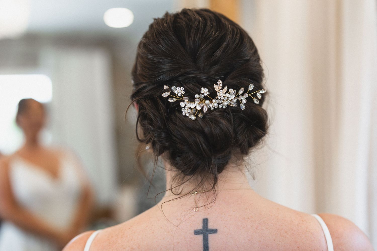 Closeup of intricate bridal hair accessory and cross tattoo on back.
