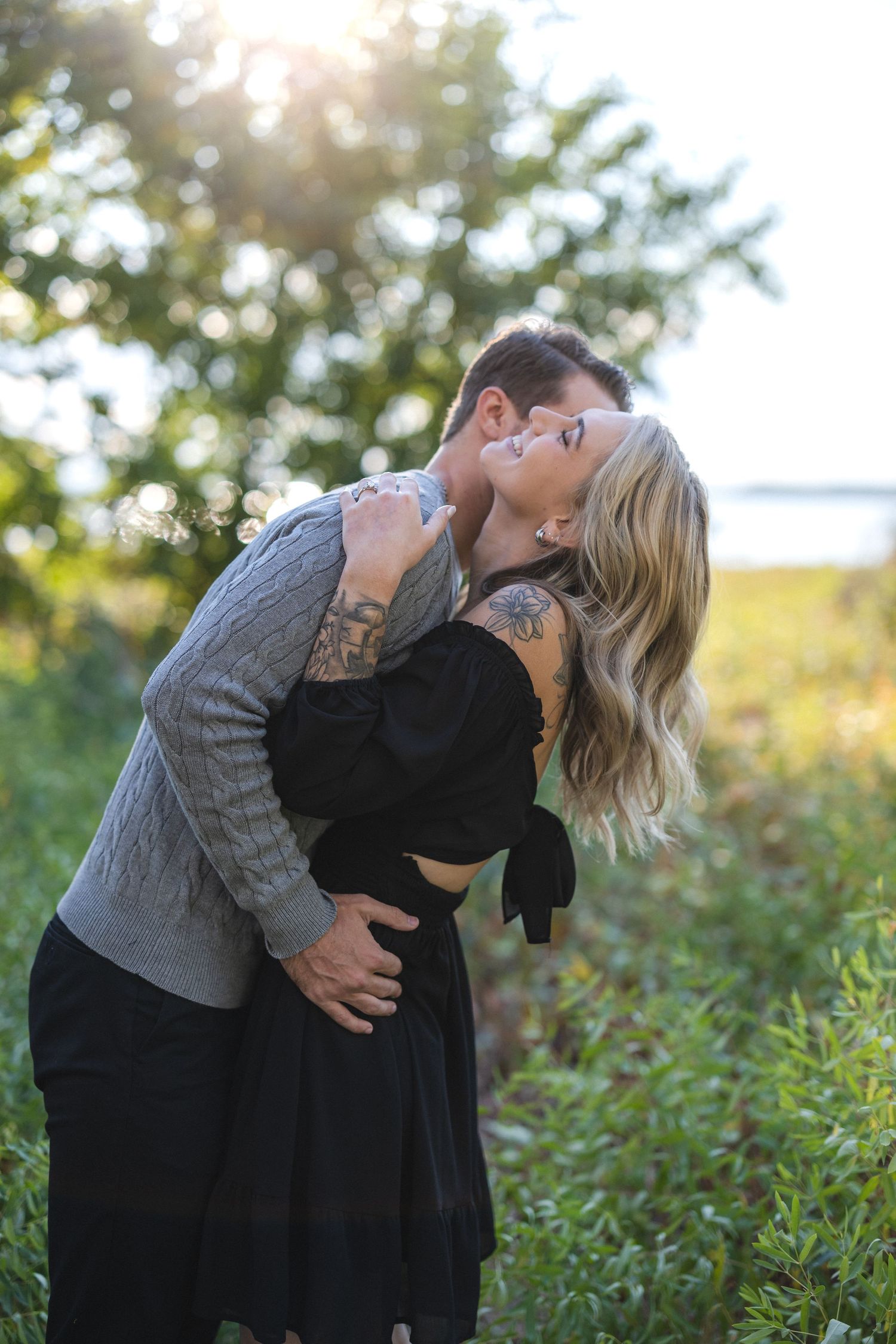 Couple sharing intimate moment in sunlit field with dramatic lighting.