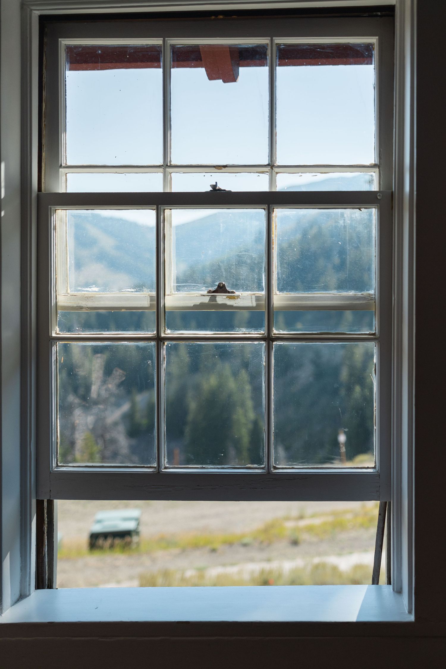 Large windows in a rustic room frame scenic mountain views with evergreen trees in the distance.