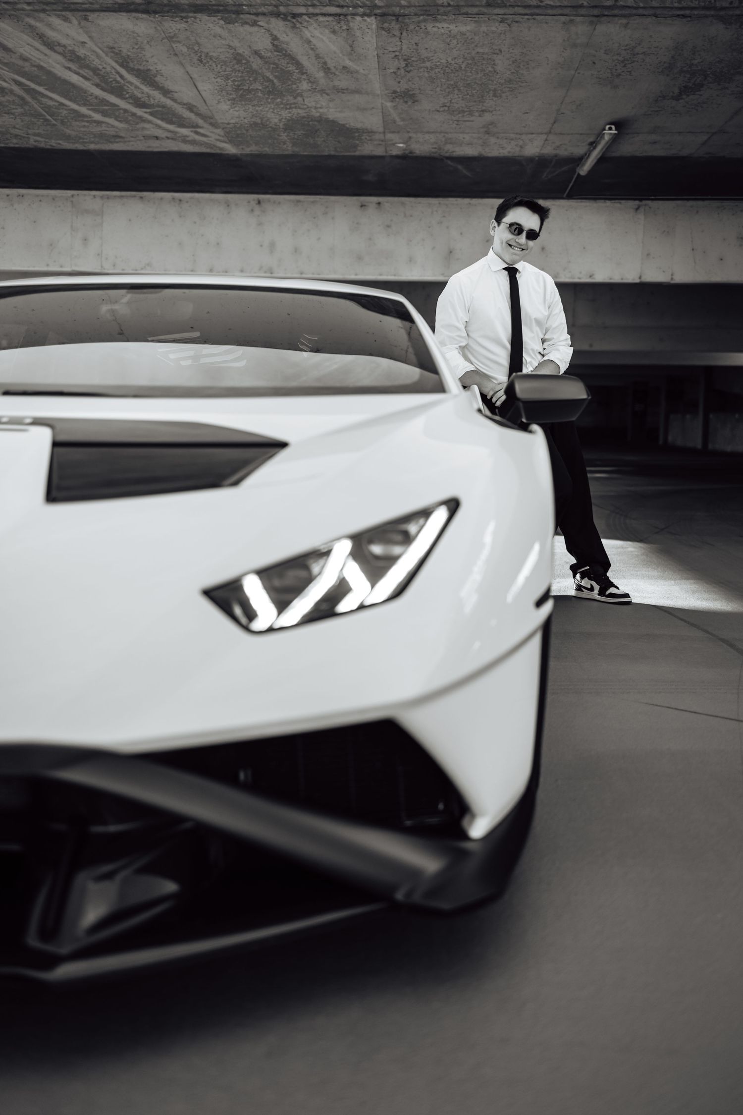 Artistic black and white shot of luxury sports car with dramatic lighting in concrete garage.