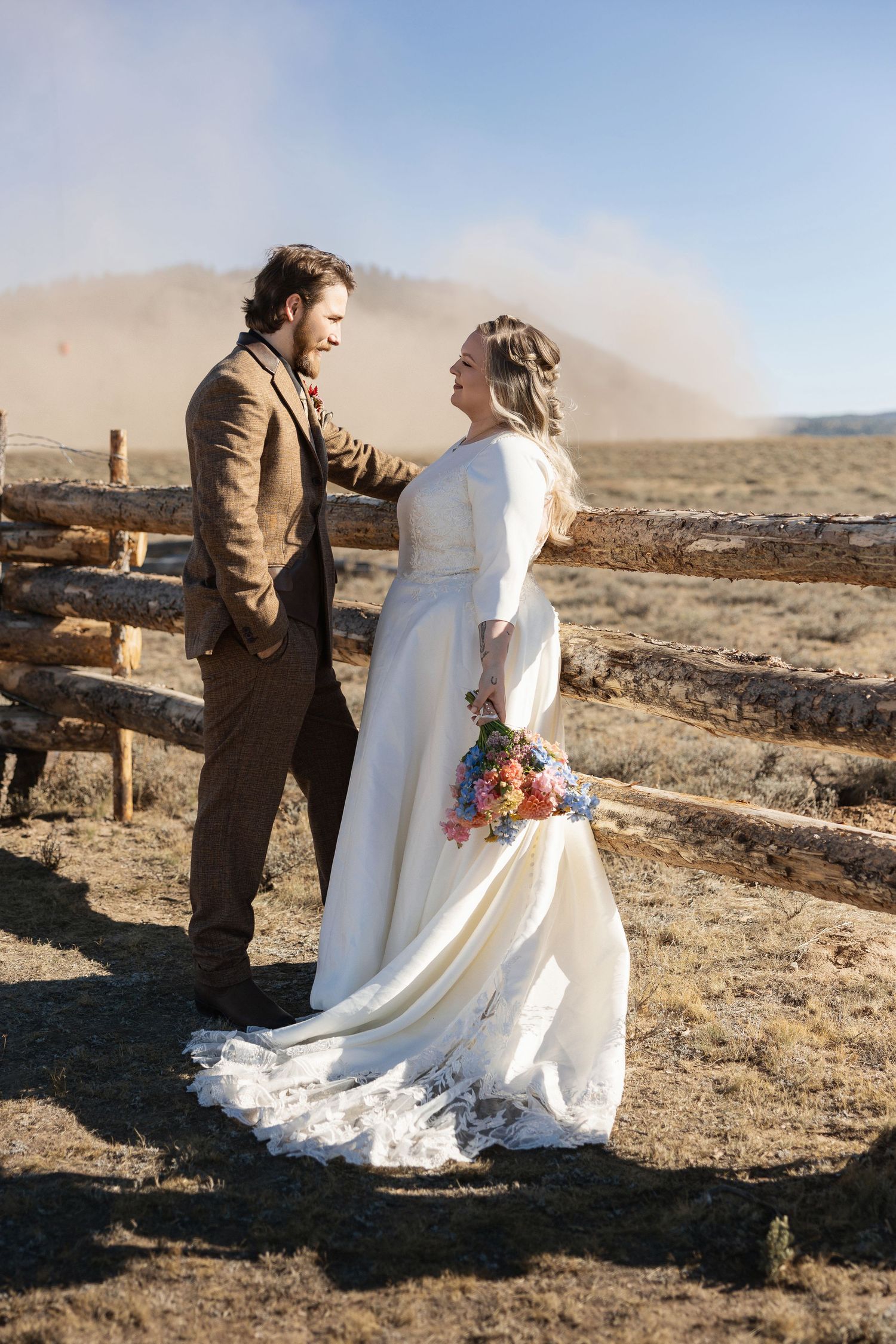 A couple shares a romantic moment in formal attire against a desert mountain backdrop.