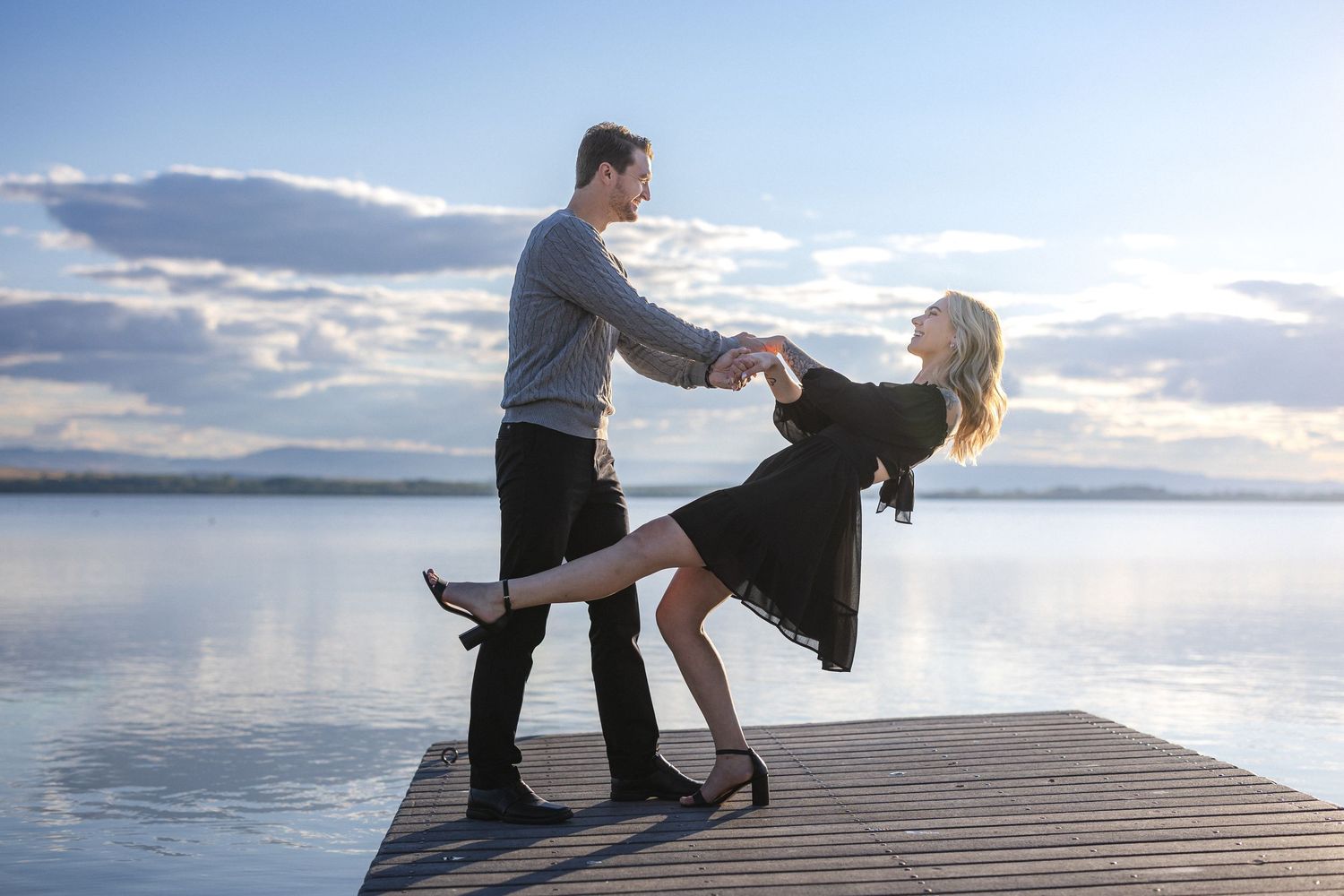 Couple shares romantic moments on wooden dock by serene lake at sunset.