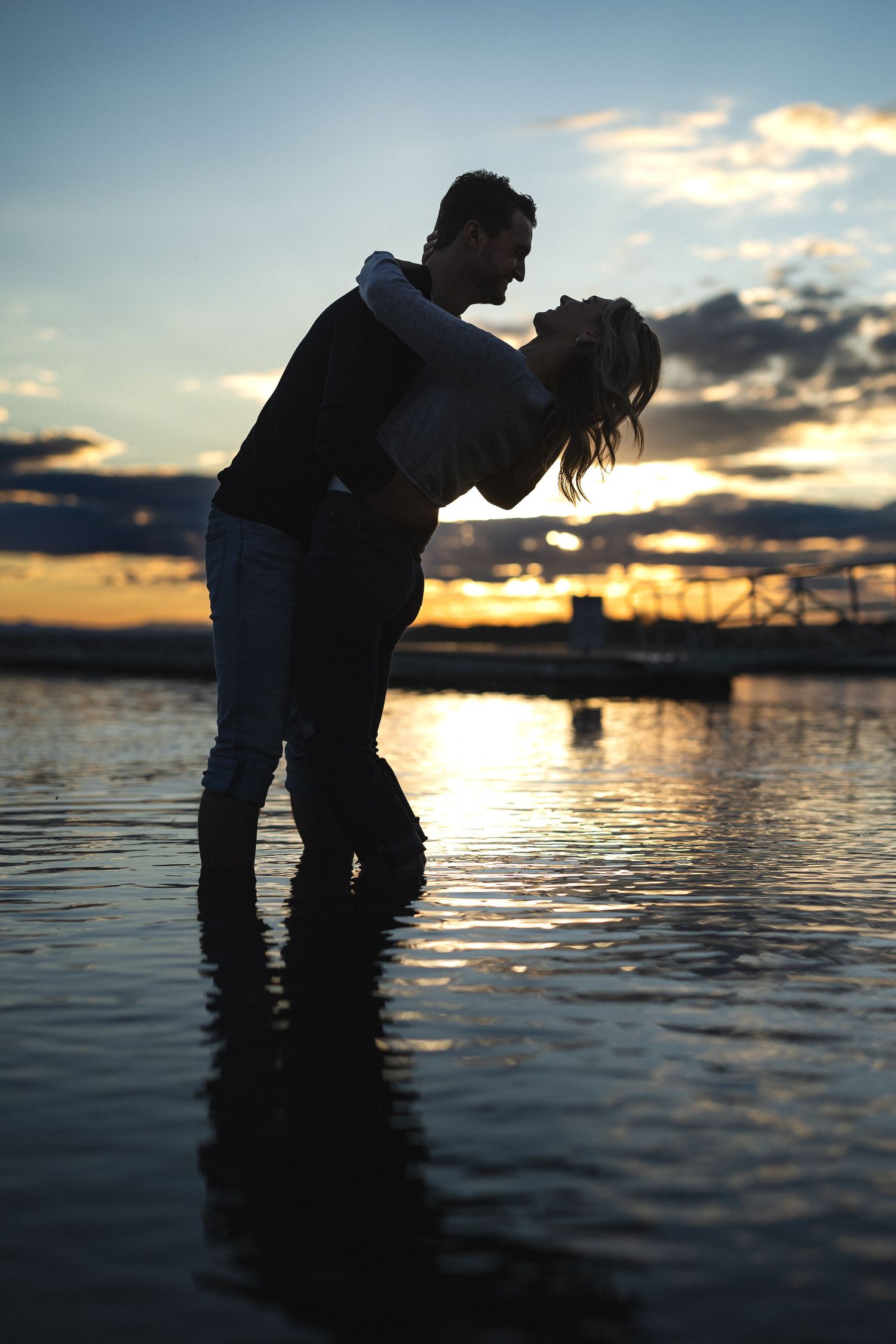 Dramatic silhouette of couple in romantic dip pose during waterfront sunset.
