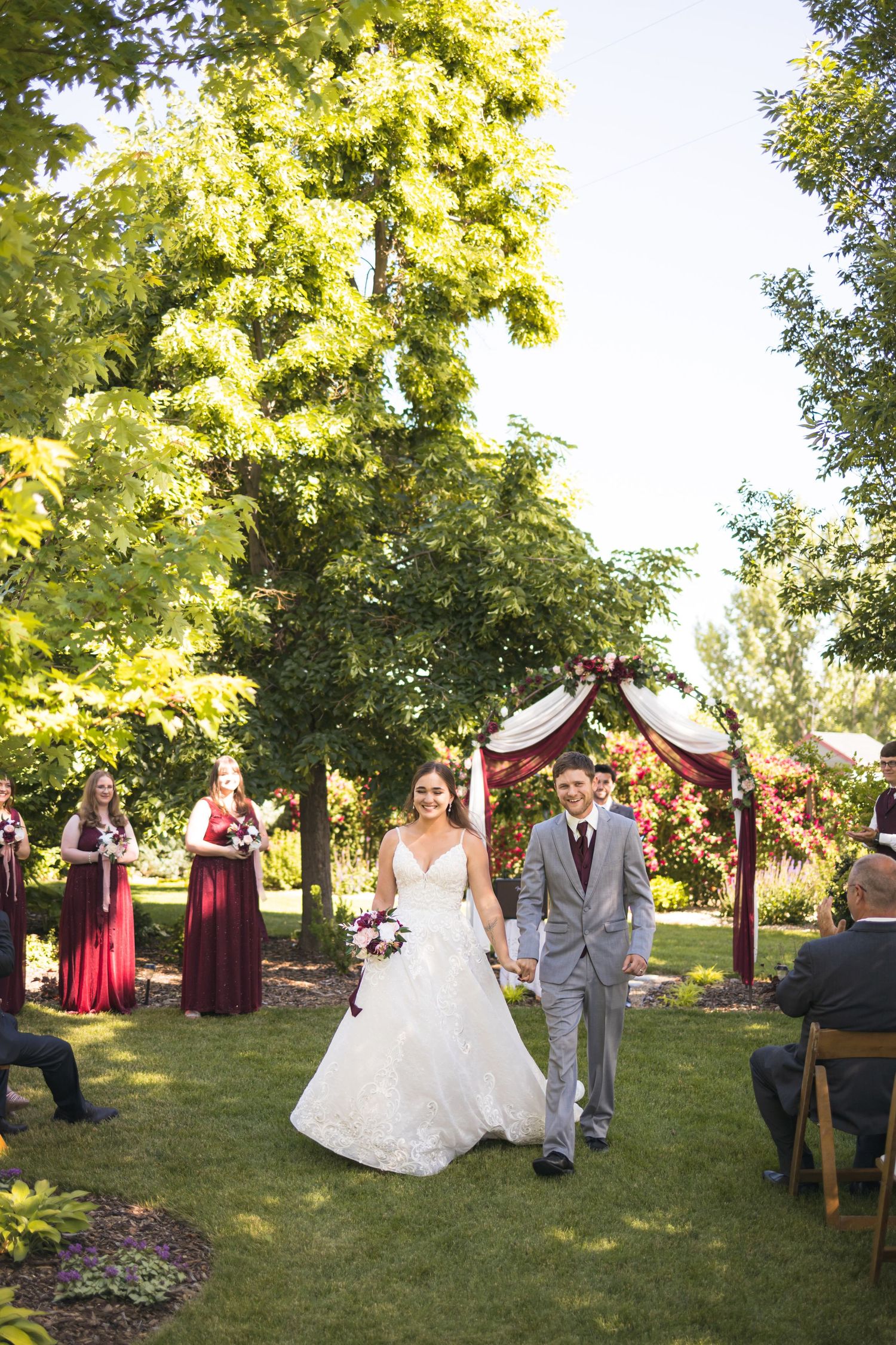 Wedding ceremony in a garden setting with couple walking down aisle under trees.