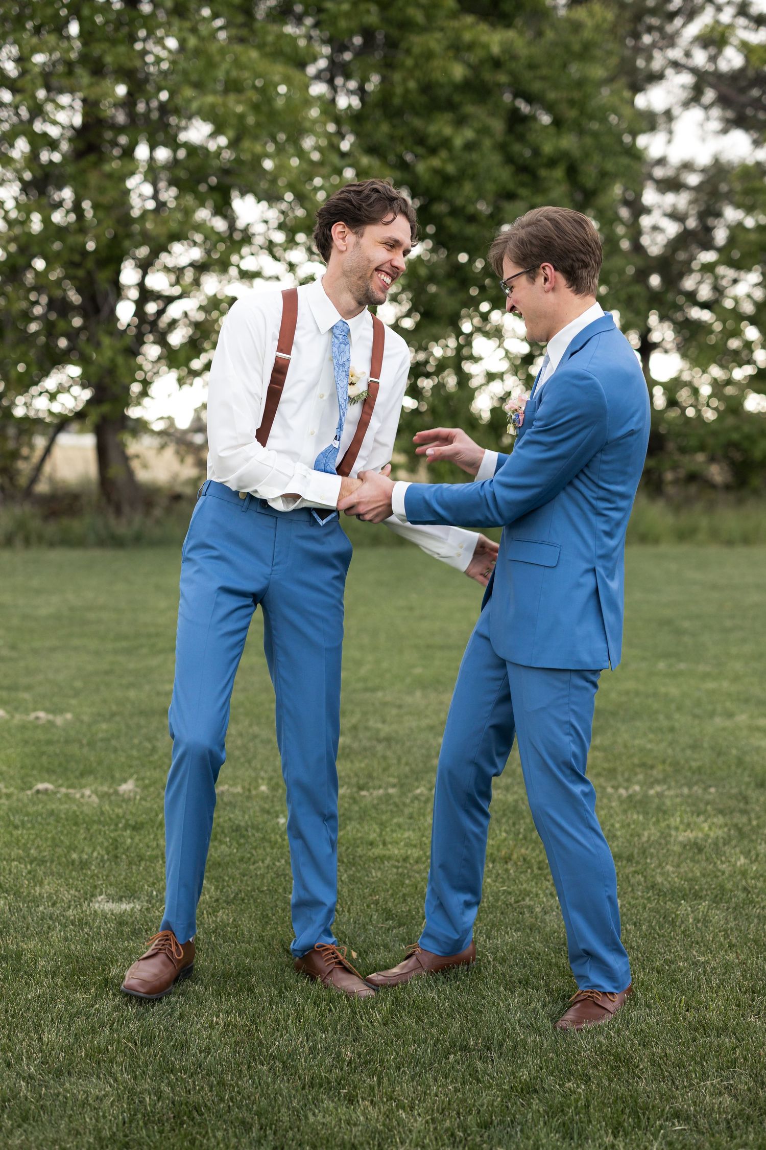 Two men in matching blue suits sharing a candid laughing moment outdoors.