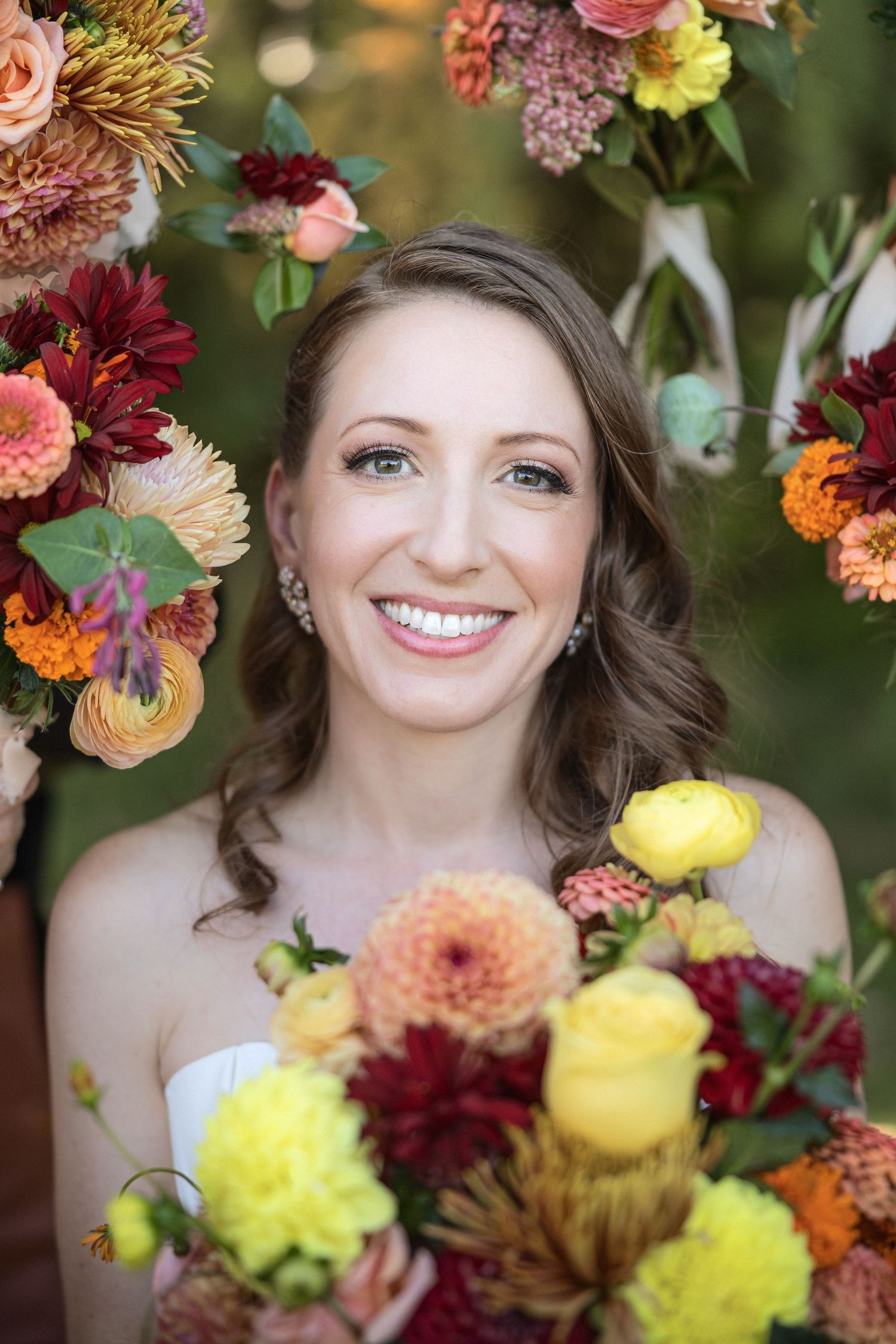 Stunning fall flowers in yellow and burgundy colors frame a close-up bridal portrait.