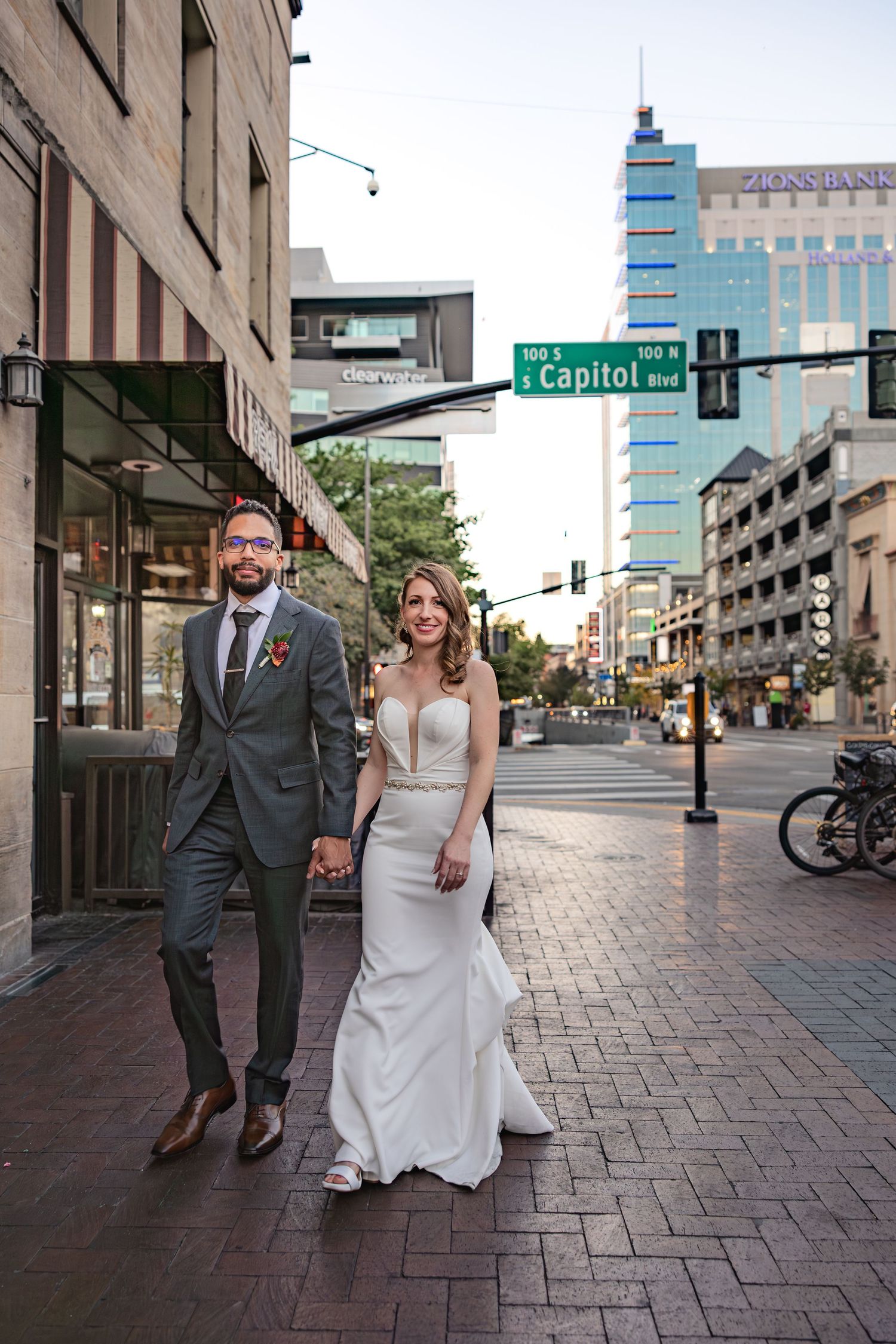 Couple in wedding attire walking down a city street with the Capitol Street sign visible.